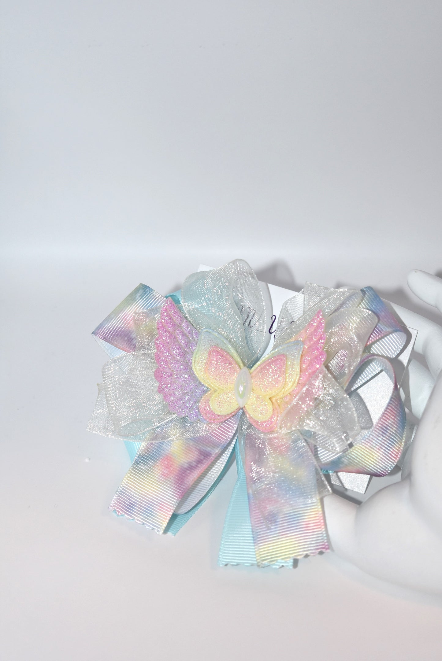 Add a splash of joy with this playful rainbow tie-dye ribbon featuring cheerful pink, blue, and yellow hues. A charming winged butterfly perches atop, bringing whimsy to your look. Securely attached to a wrapped alligator clip, it’s perfect for brightening any outfit with a touch of fun and color.