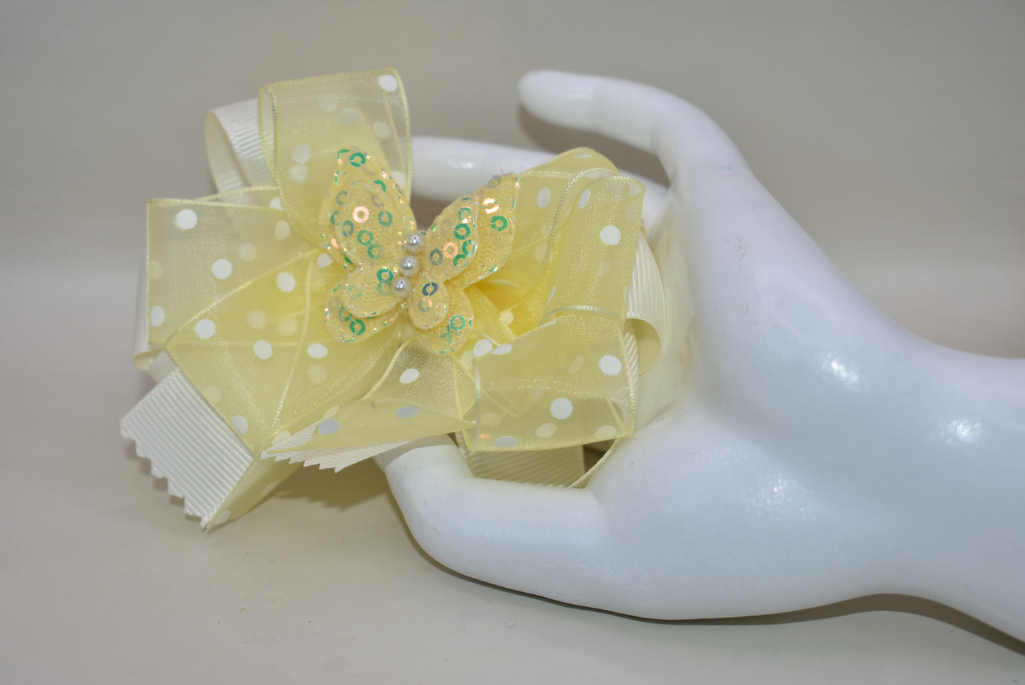 Add a splash of sunshine with this adorable bow from Nana's Collection! 🌼 Soft baby yellow grosgrain and delicate organza ribbons tie together a playful polka dot bow, topped with a sparkly butterfly 🦋. Secured with a wrapped alligator clip, it stays put for all-day fun. Perfect for brightening any outfit with a touch of charm and sparkle! ✨