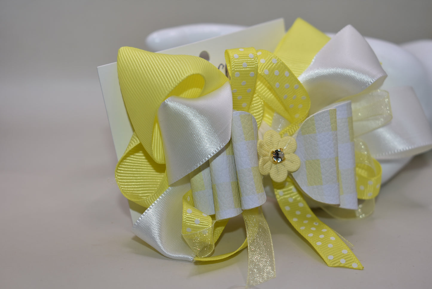 Add a splash of sunshine to your look with this playful hair clip from Nana's Collection 166. Featuring a cheerful mix of yellow and white ribbons accented with charming polka dots, it’s topped with a cute yellow flower and sparkling crystal for a touch of sparkle. The wrapped alligator clip ensures a secure hold, making it perfect for brightening any hairstyle with a fun, whimsical flair.