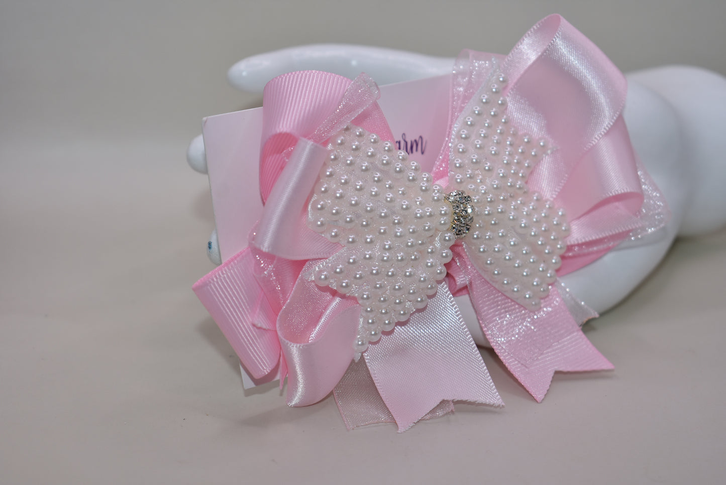 Add a splash of charm with this beautiful pink bow from Nana's Collection! 🌸 Layers of soft pink ribbons create a perfect princess look, topped with a sparkling pearl and crystal wrap ✨. The wrapped alligator clip makes it super easy to wear all day long. Perfect for the little girl who loves everything pink and pretty! 🎀💕