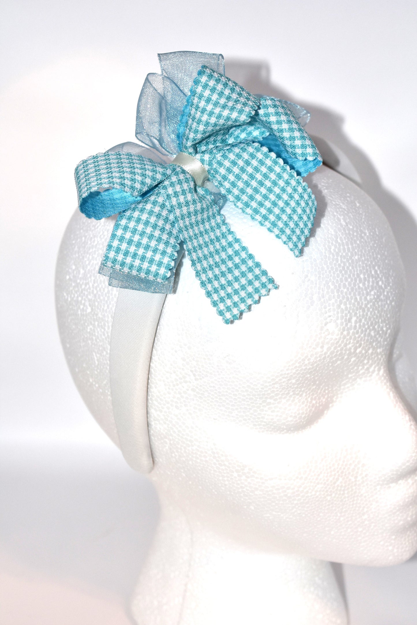 Add a splash of charm with this soft off-white headband topped with a cheerful aqua checkered ribbon. Lightweight and comfy, it’s perfect for all-day wear while adding a playful touch to any outfit.