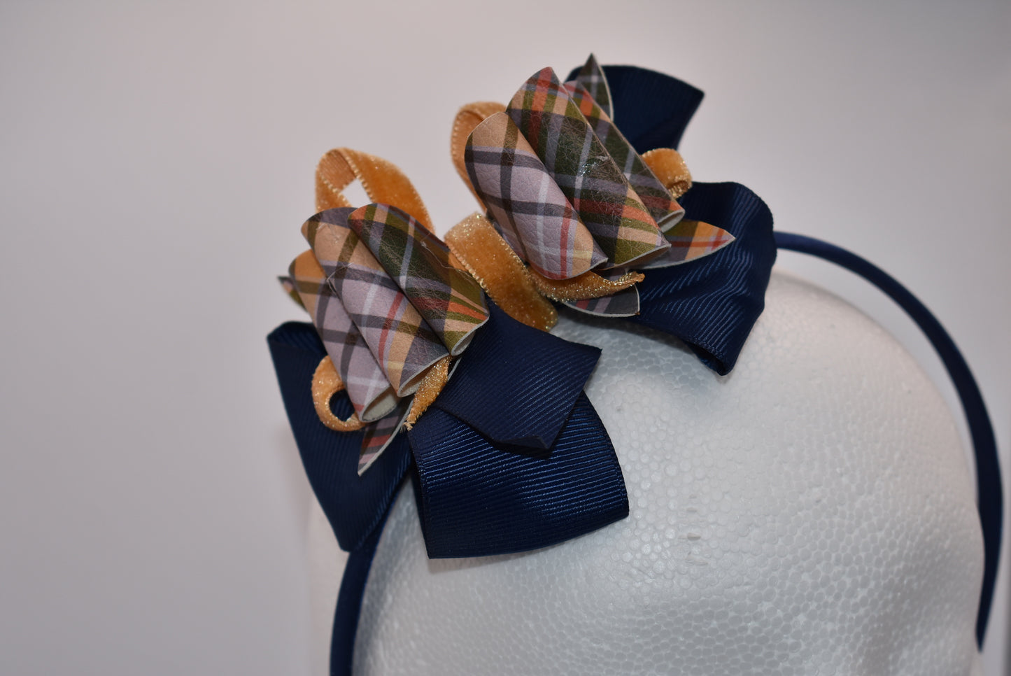 Add a splash of autumn charm with this navy blue satin headband from Nana's Headband Collection. Featuring a playful faux leather bow in gold and blue patterns layered with fun ribbons, it brings comfort and style perfectly suited for your little one’s fall adven