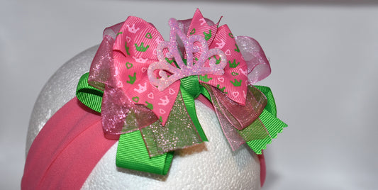This one-of-a-kind wide headband features soft pink nylon for all-day comfort. Its adorable pink and green ribbon is topped with a playful princess bow and crown, adding a magical touch. Perfect for anyone young or old who loves a fun, charming accessory.
