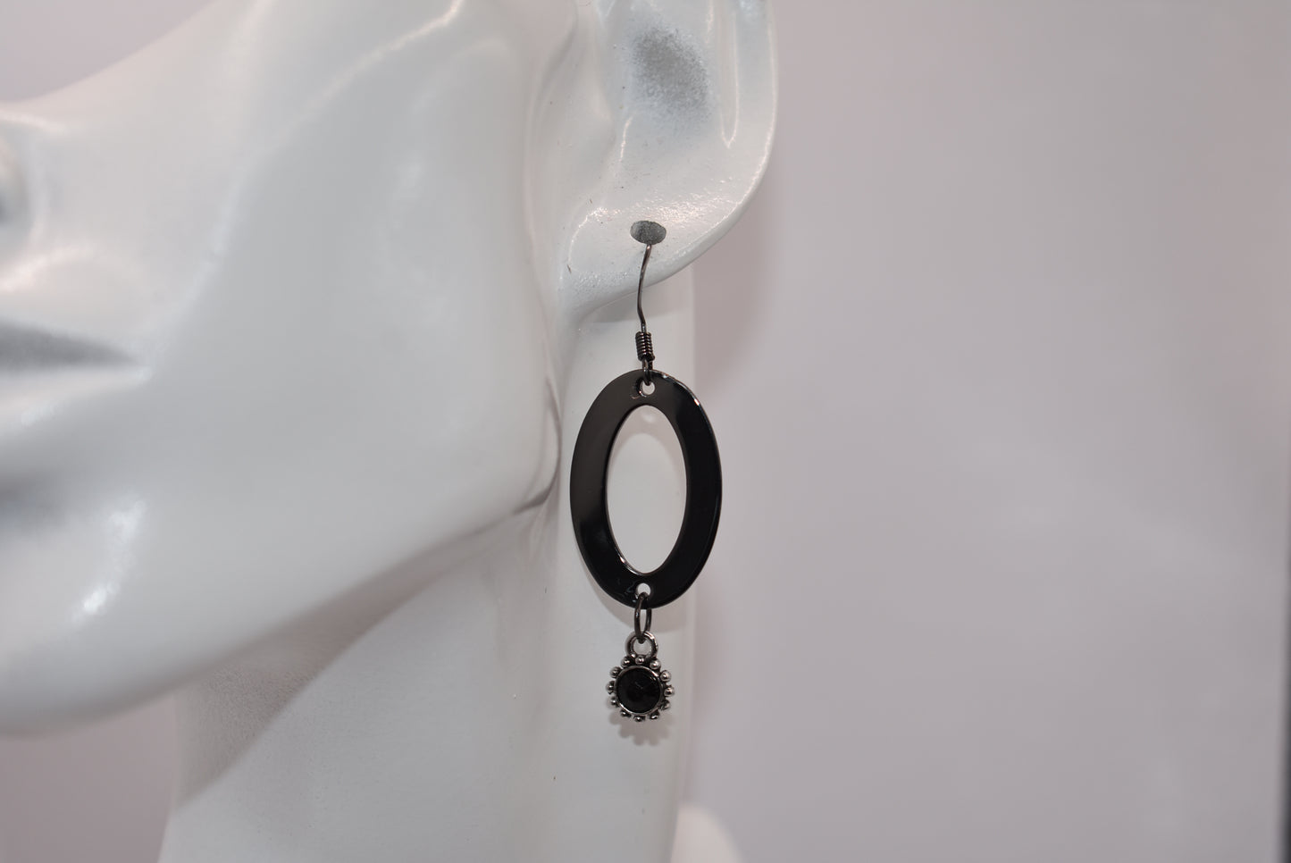 "Sleek, stylish, and hypoallergenic, our Black Collection features black hooks that hold a polished black oval shaped piece with a stunning silver/black charm and center stone hanging from the bottom.  Perfect for adding a touch of edgy elegance to any outfit. (Definitely not your average black jewelry.)"