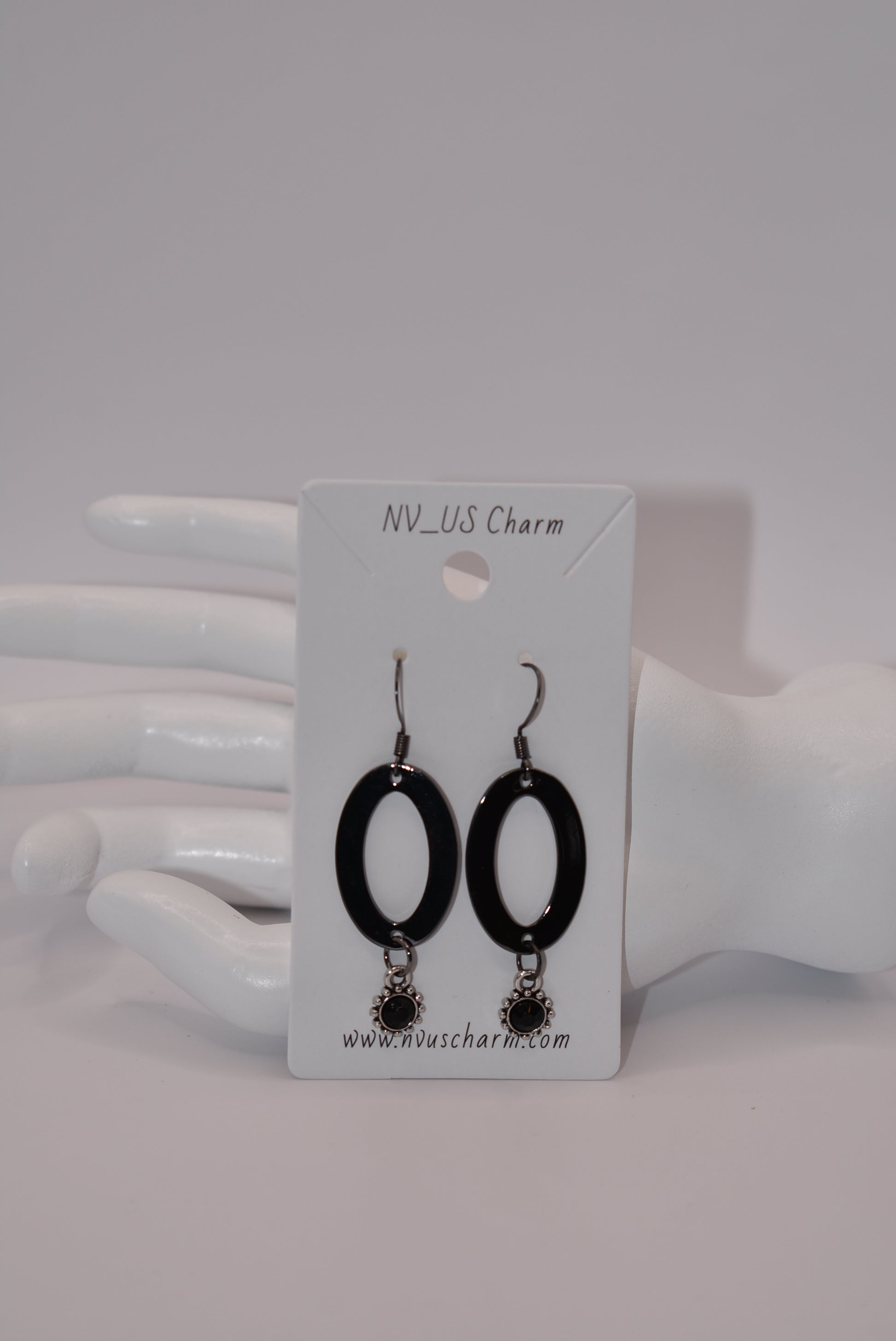 "Sleek, stylish, and hypoallergenic, our Black Collection features black hooks that hold a polished black oval shaped piece with a stunning silver/black charm and center stone hanging from the bottom.  Perfect for adding a touch of edgy elegance to any outfit. (Definitely not your average black jewelry.)"