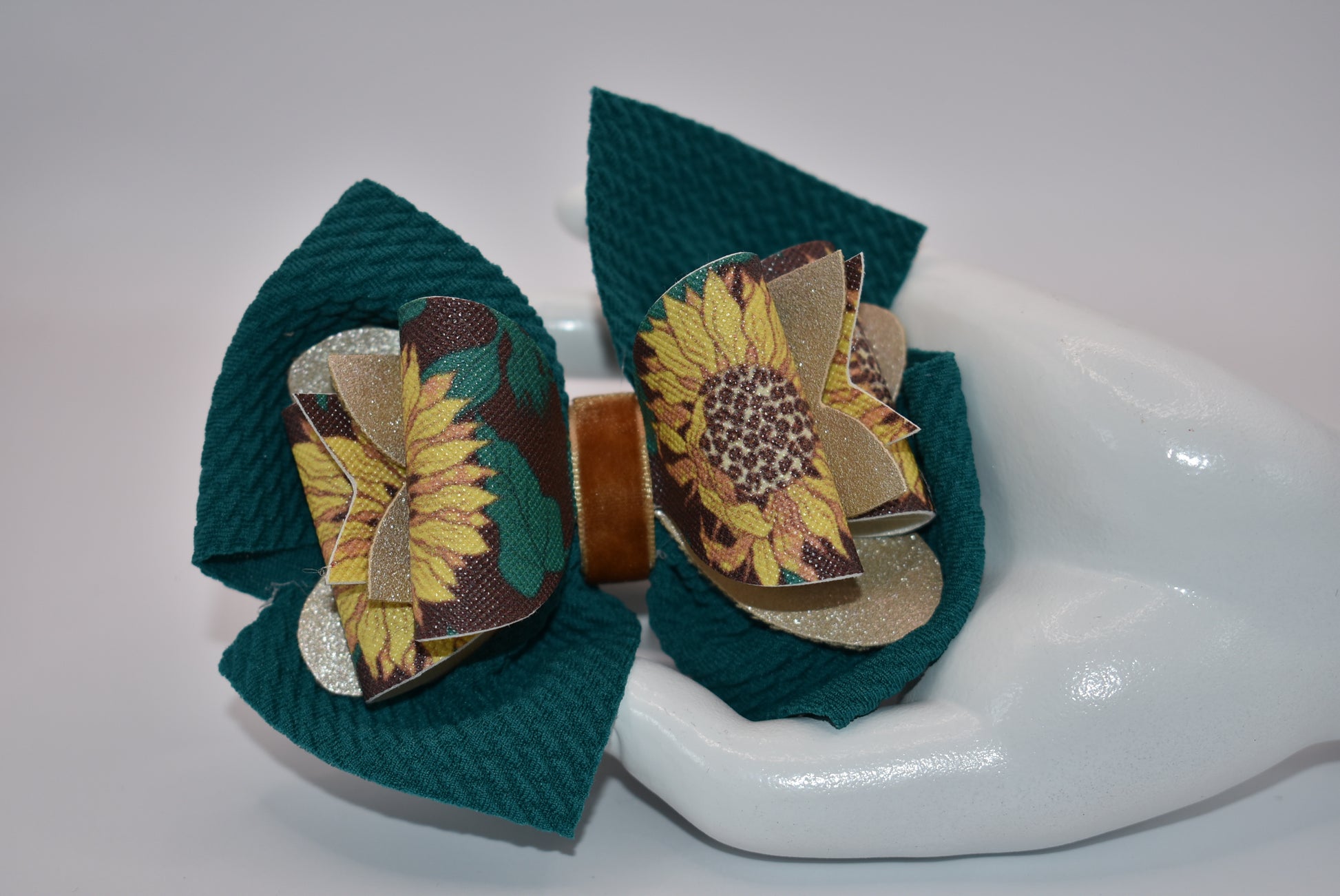 Experience the beauty of fall with Nana's Collection! This Hunter Green bow features a faux leather sunflower motif on top, adding a touch of elegance. The velvet center provides comfort and the alligator clip allows for easy placement. Get ready to turn heads with this stylish accessory!