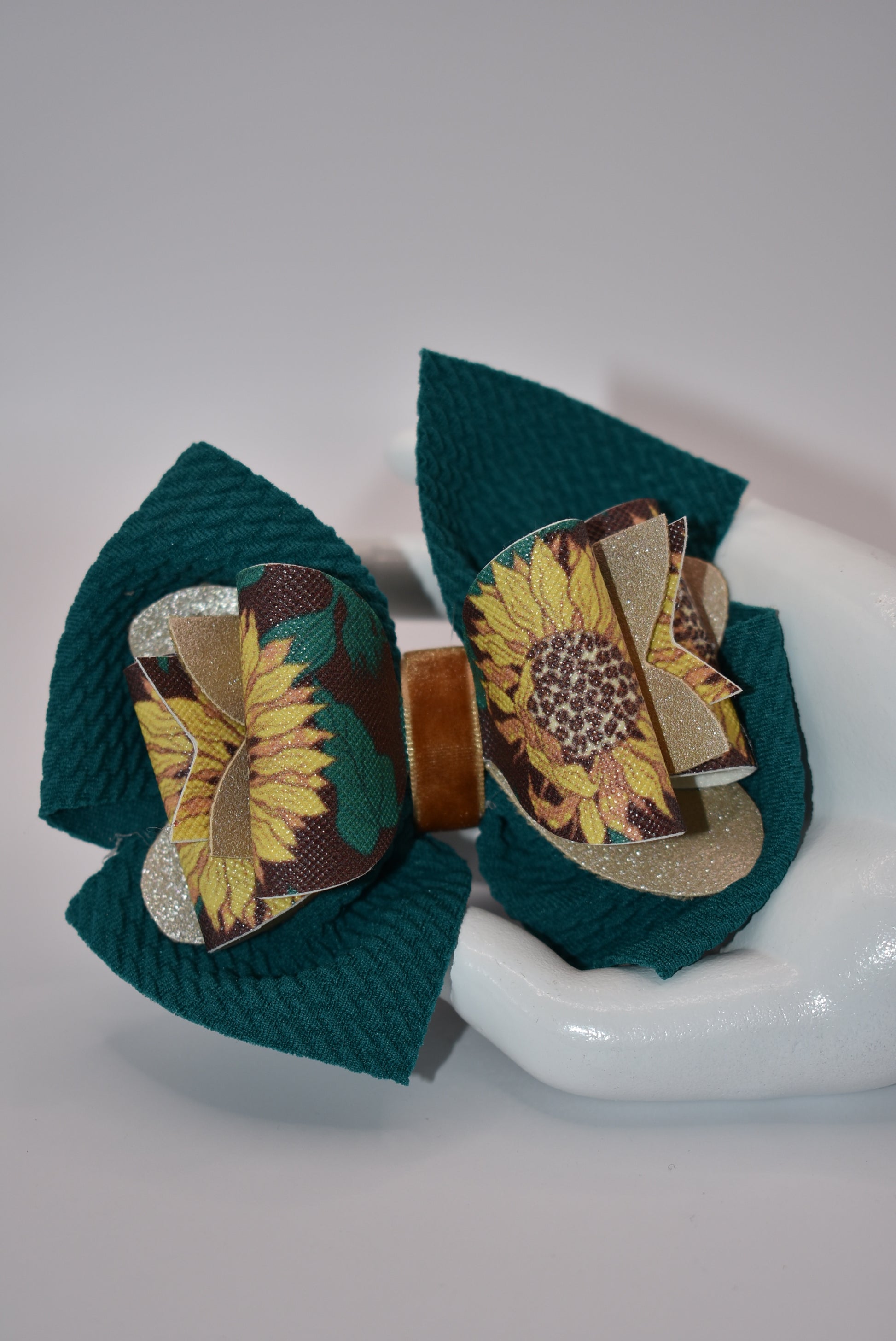 Experience the beauty of fall with Nana's Collection! This Hunter Green bow features a faux leather sunflower motif on top, adding a touch of elegance. The velvet center provides comfort and the alligator clip allows for easy placement. Get ready to turn heads with this stylish accessory!