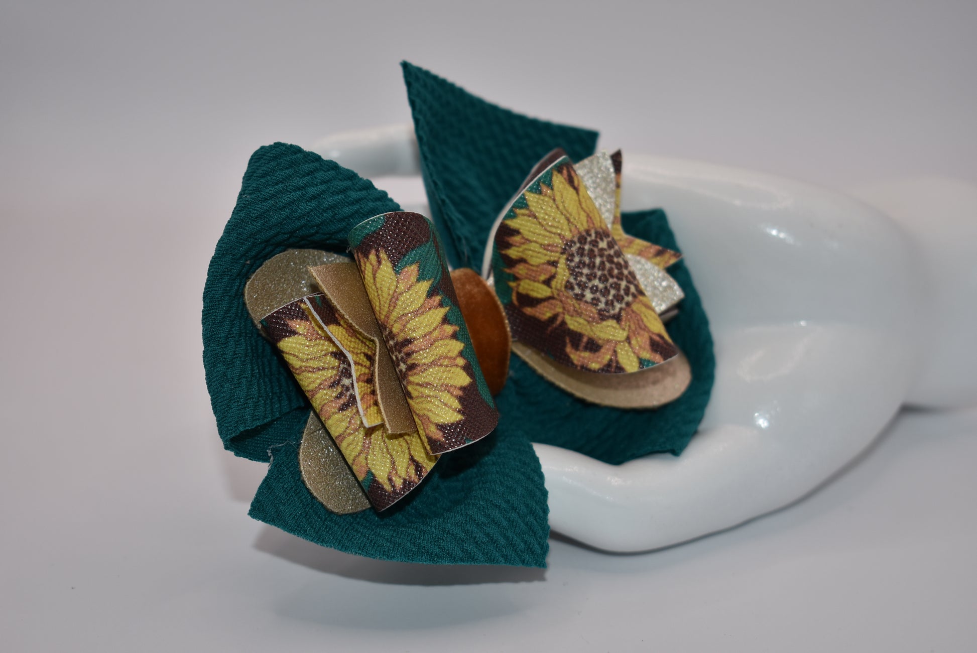 Experience the beauty of fall with Nana's Collection! This Hunter Green bow features a faux leather sunflower motif on top, adding a touch of elegance. The velvet center provides comfort and the alligator clip allows for easy placement. Get ready to turn heads with this stylish accessory!