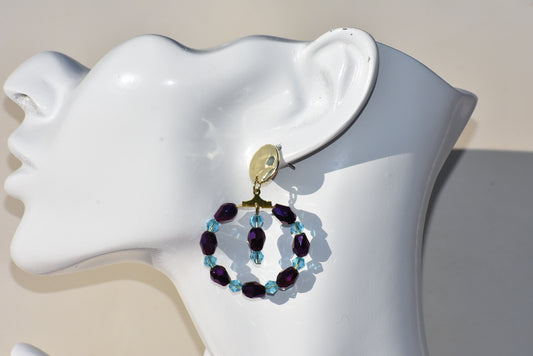 Add a pop of color to your ensemble with our Purple Collection! This one-of-a-kind piece features stunning purple and aqua crystals, surrounding a circle hanging design. The gold filled hypoallergenic posts ensure a comfortable and stylish fit. Stand out with this unique accessory!