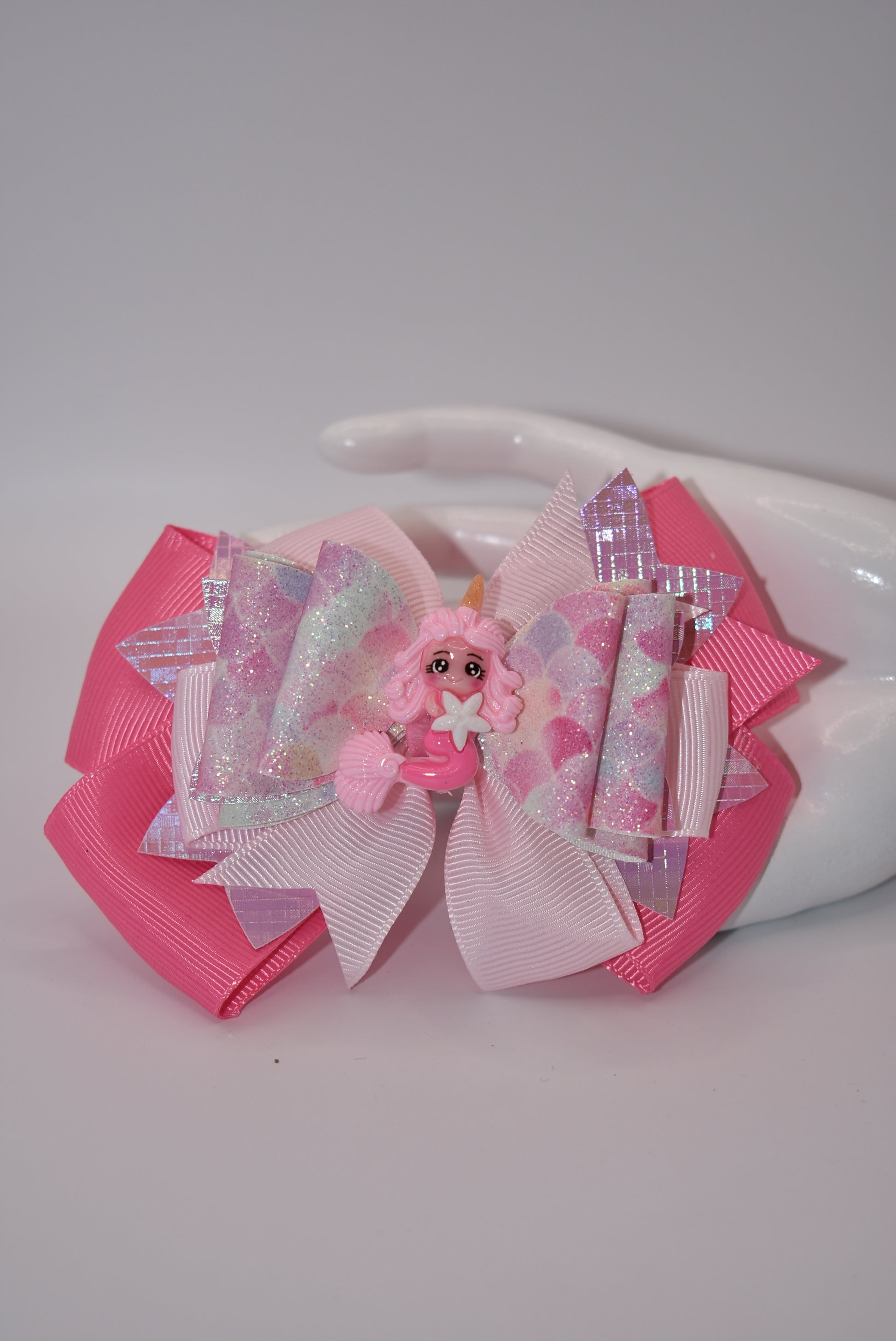 Add a touch of whimsy and sparkle to any outfit with Nana's Collection. This textured faux leather bow, in the prettiest shade of pink, features a playful mermaid design and layers of fun. The alligator clip ensures comfortable wear, while the pink ribbon bow adds a perfect finishing touch.