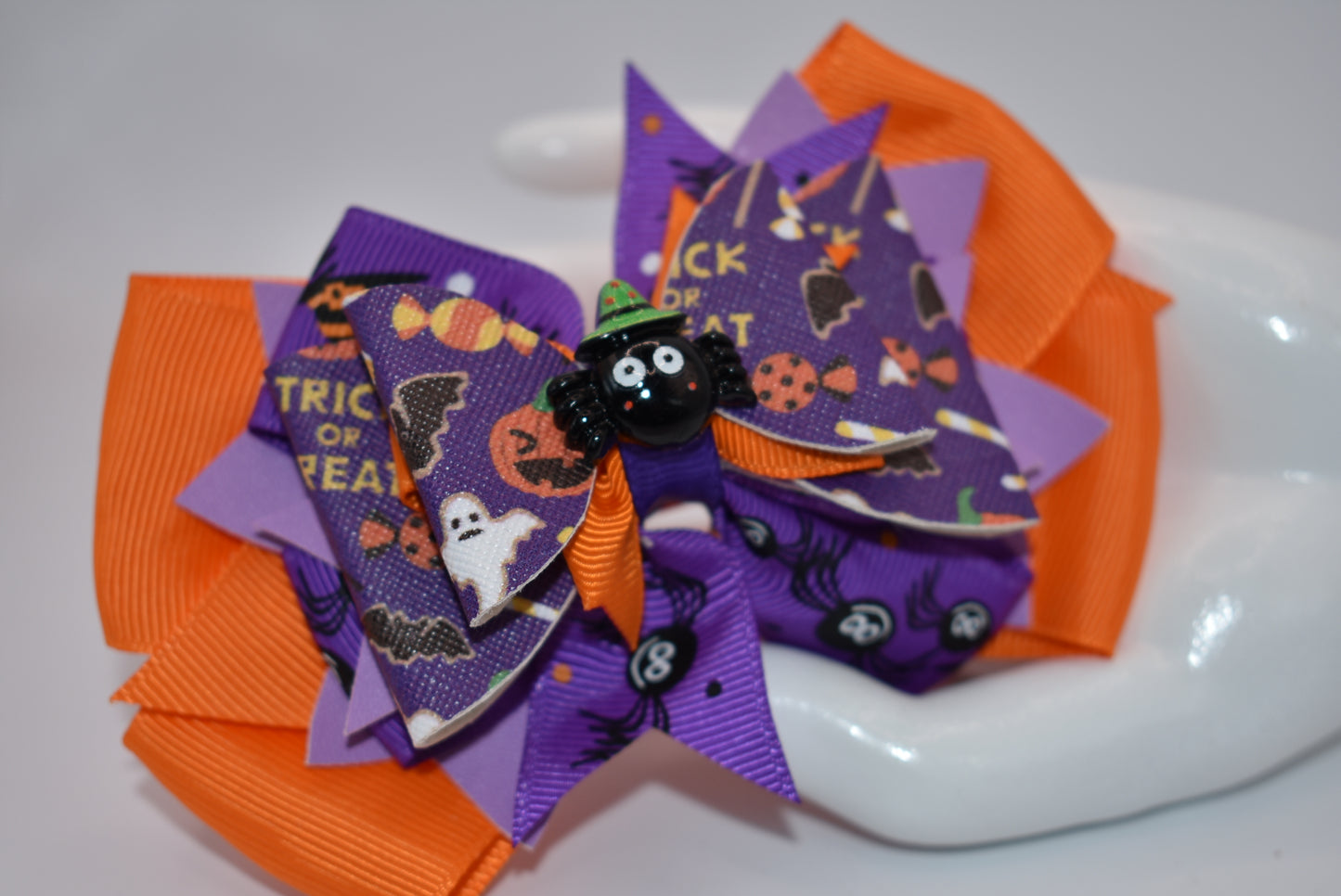 Add a playful touch to your Halloween outfit with our Nana's Collection! This super fun bow features plenty of purple, orange, and black colors, along with a cute Halloween charm on top. The alligator clip ensures comfort while adding a quirky, spooky element.