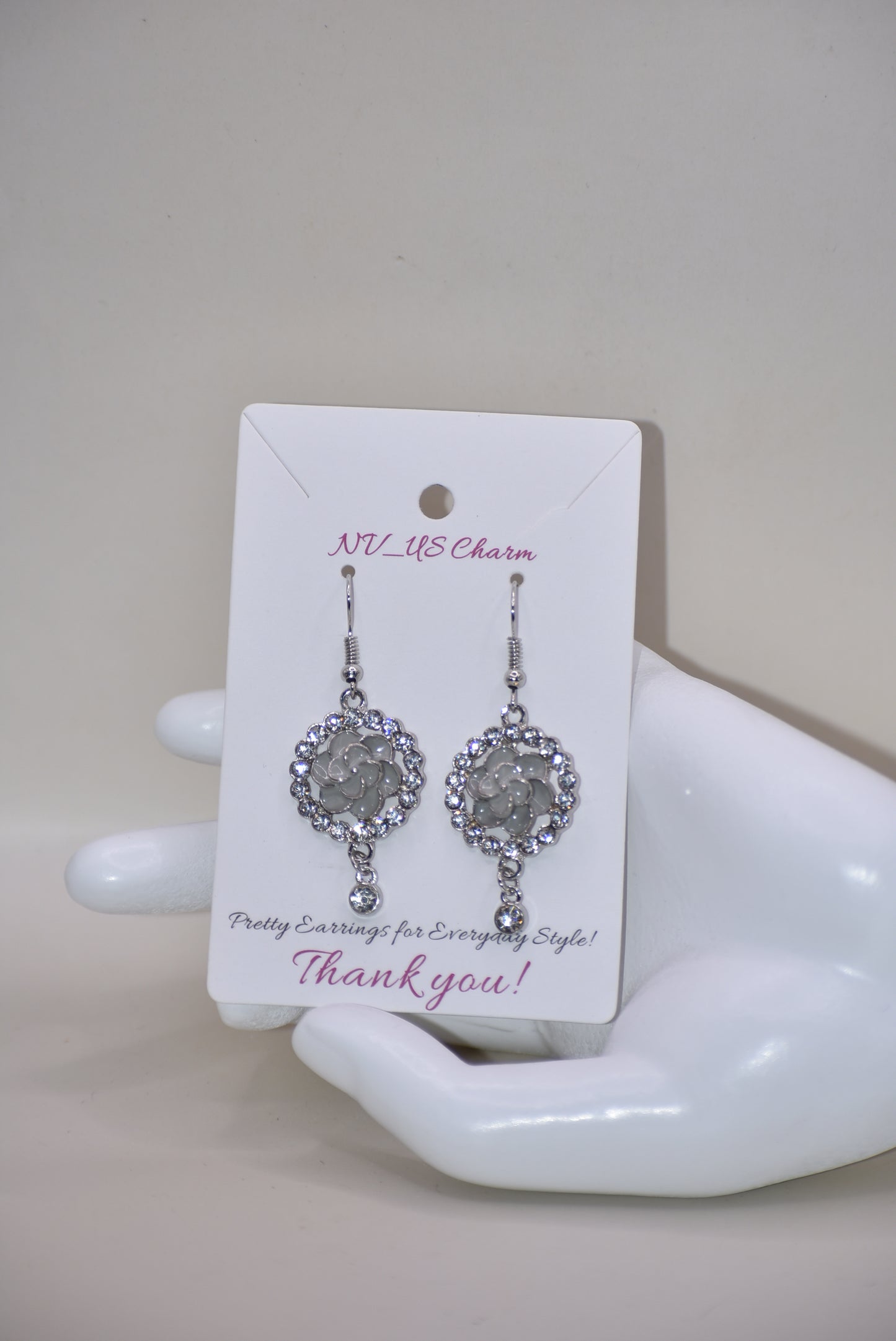 These Gray Collection 9 earrings provide a unique and sophisticated look. Featuring a pretty gray flower surrounded by crystals and a small crystal hanging, these silver hook earrings will add sparkle and elegance to any outfit. With intricate details and luxurious design, these earrings are a must-have addition to any jewelry collection.