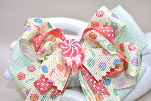Add a pop of fun to your hair with Nana's Collection 66! Featuring a super fun lollipop bow with a cute charm on top, this ribbon combination of green and peach will make you stand out. The wrapped alligator clip adds comfort for all-day wear. 😍