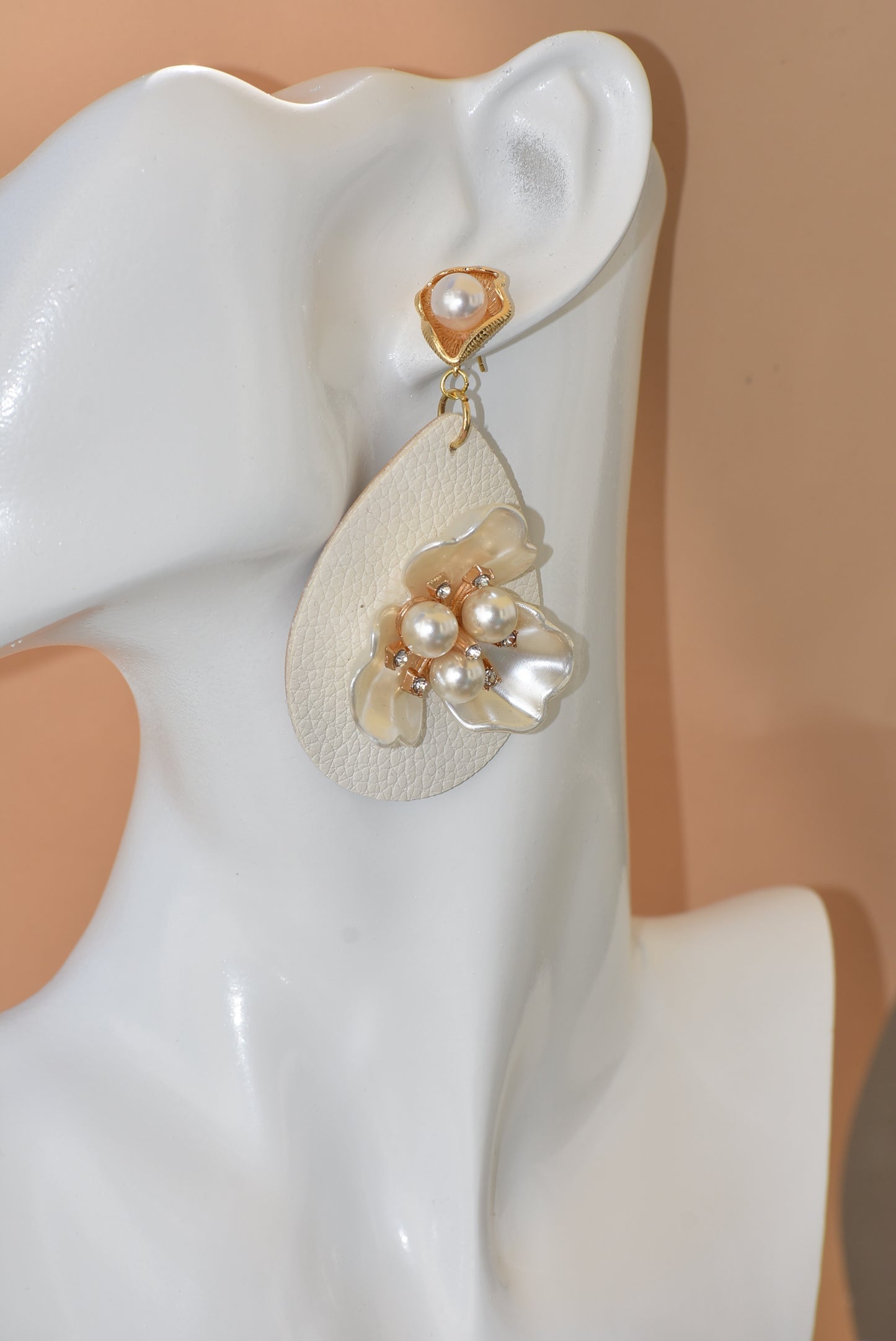 Immerse yourself in one-of-a-kind beauty with the Wedding Collection 5 earrings. Blending a cream faux leather teardrop with a stunning pearl flower center, these earrings will set you apart from everyone else. They hang from gold pearl posts for comfort, making them perfect for any special occasion.