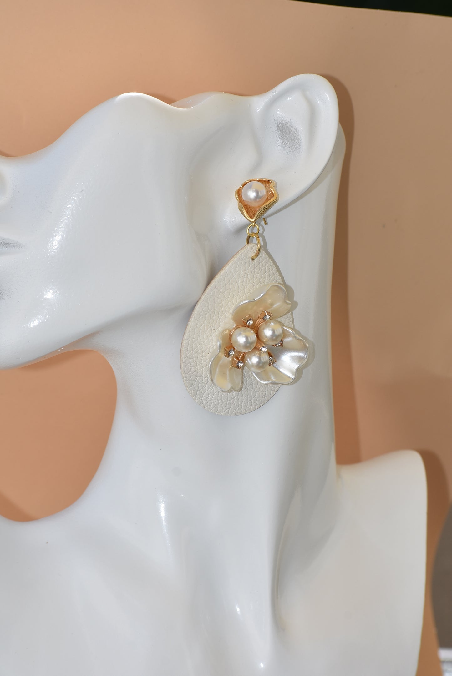 Immerse yourself in one-of-a-kind beauty with the Wedding Collection 5 earrings. Blending a cream faux leather teardrop with a stunning pearl flower center, these earrings will set you apart from everyone else. They hang from gold pearl posts for comfort, making them perfect for any special occasion.