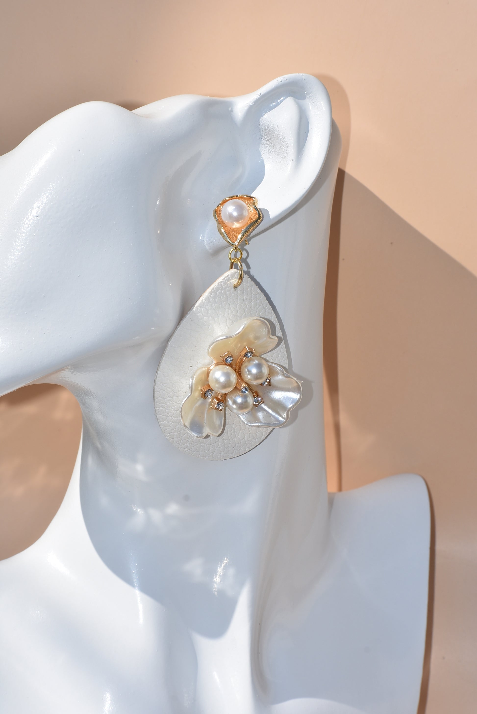 Immerse yourself in one-of-a-kind beauty with the Wedding Collection 5 earrings. Blending a cream faux leather teardrop with a stunning pearl flower center, these earrings will set you apart from everyone else. They hang from gold pearl posts for comfort, making them perfect for any special occasion.