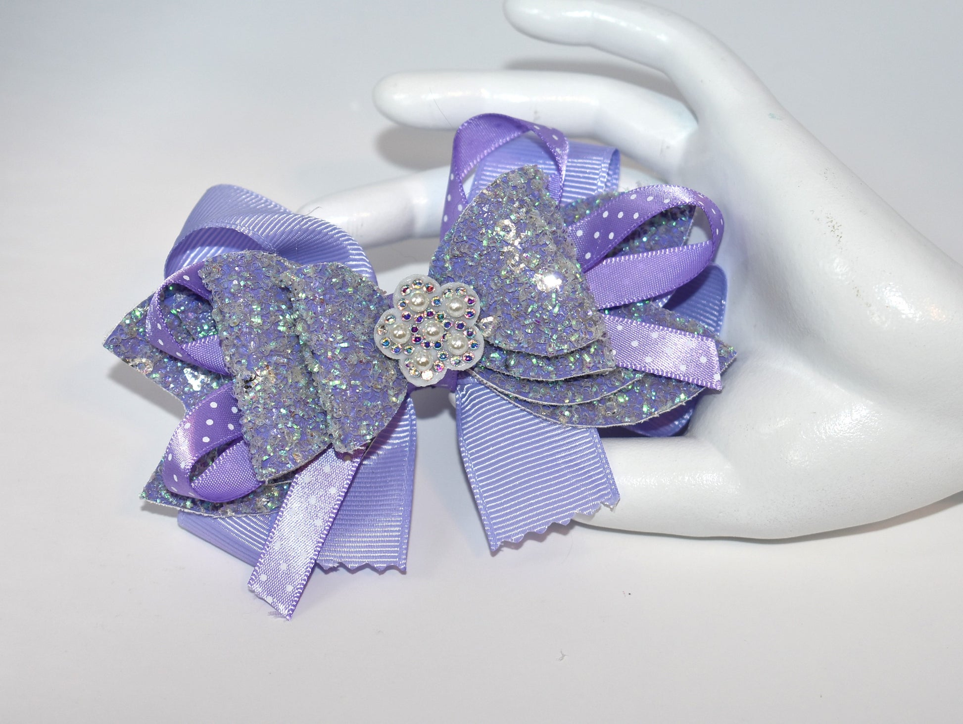 Add a splash of charm with this delightful accessory featuring a pretty lavender ribbon and sparkly faux leather, accented by a touch of purple satin polka dot ribbon 🎀. A shiny flower and a lovely pearl top it off for extra sparkle ✨. The alligator clip ensures a secure fit, wrapped comfortably for all-day wear. Perfect for adding a playful pop to any outfit! 🌸💜