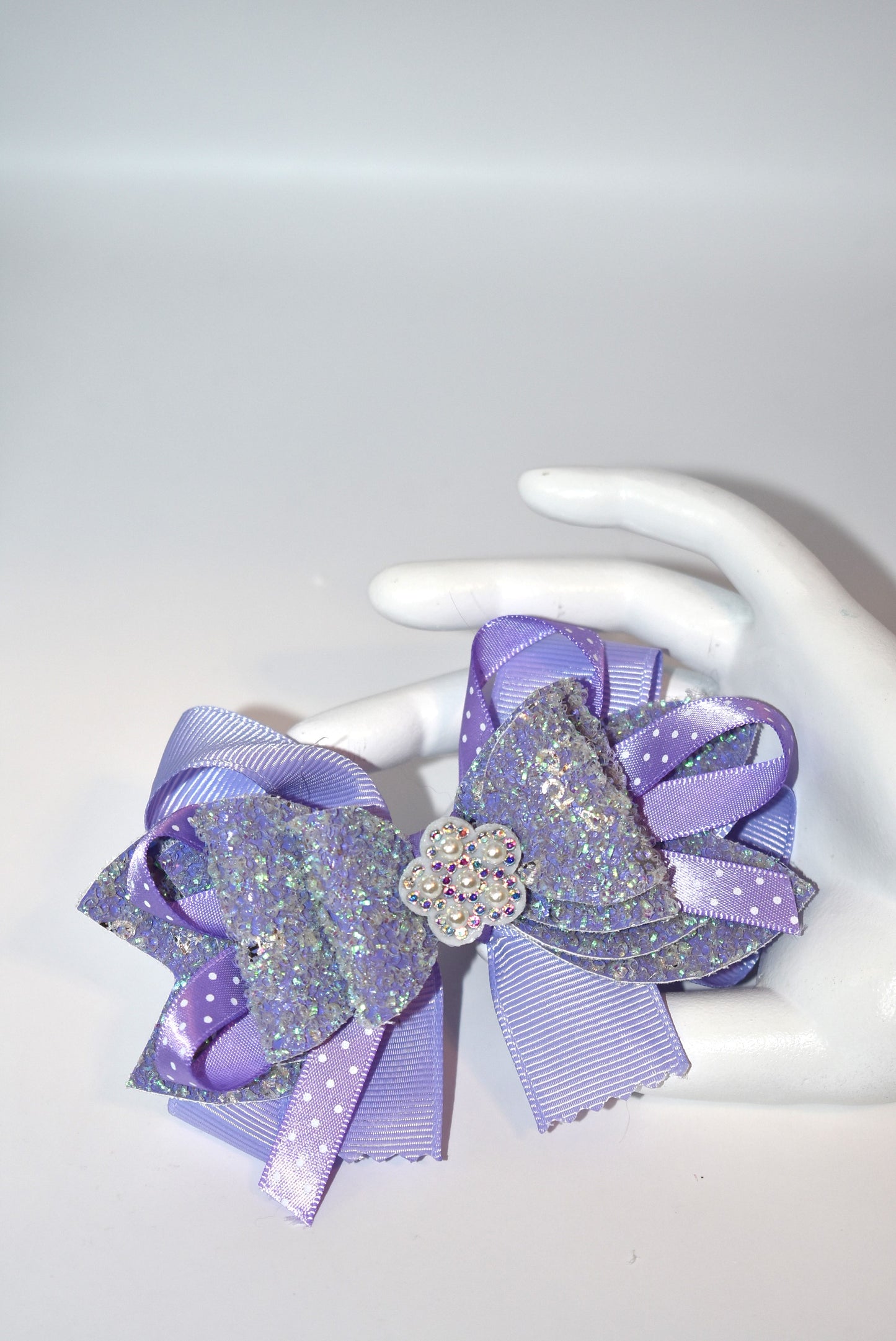 Add a splash of charm with this delightful accessory featuring a pretty lavender ribbon and sparkly faux leather, accented by a touch of purple satin polka dot ribbon 🎀. A shiny flower and a lovely pearl top it off for extra sparkle ✨. The alligator clip ensures a secure fit, wrapped comfortably for all-day wear. Perfect for adding a playful pop to any outfit! 🌸💜