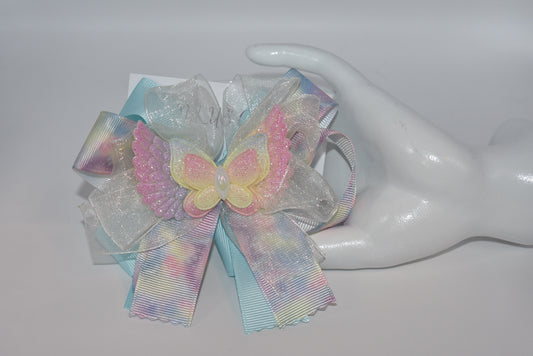 Add a splash of joy with this playful rainbow tie-dye ribbon featuring cheerful pink, blue, and yellow hues. A charming winged butterfly perches atop, bringing whimsy to your look. Securely attached to a wrapped alligator clip, it’s perfect for brightening any outfit with a touch of fun and color.