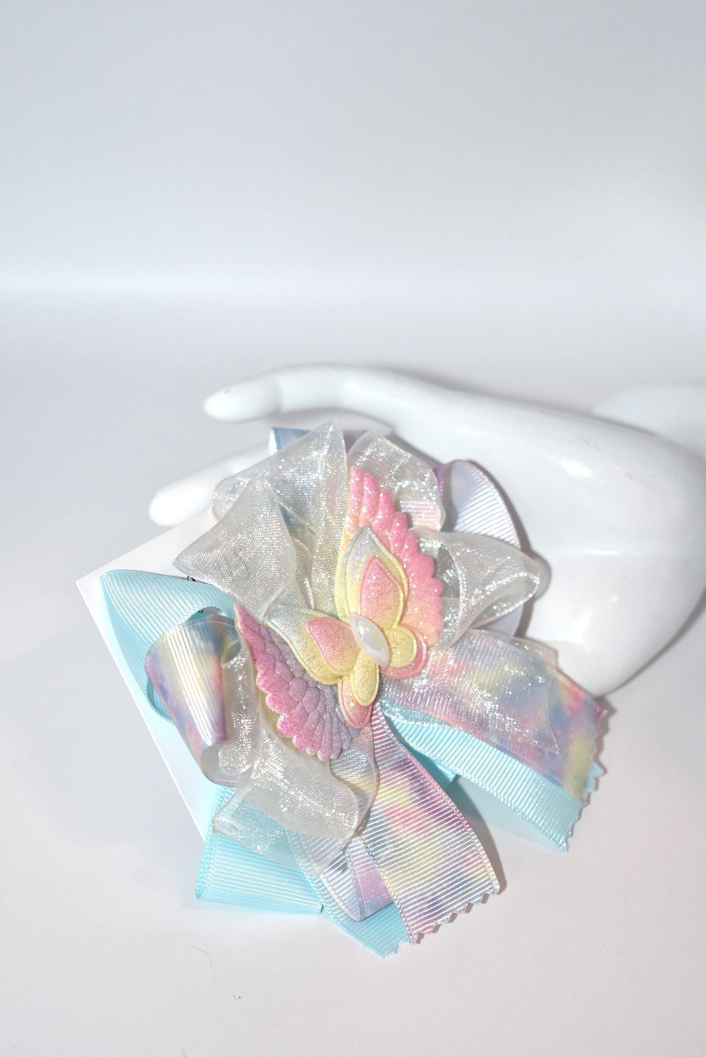 Add a splash of joy with this playful rainbow tie-dye ribbon featuring cheerful pink, blue, and yellow hues. A charming winged butterfly perches atop, bringing whimsy to your look. Securely attached to a wrapped alligator clip, it’s perfect for brightening any outfit with a touch of fun and color.