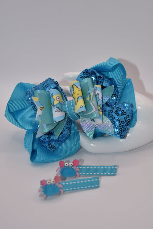 Get ready to make a splash with Nana's Collection! Our Under the Sea Bow features a playful crab-inspired design mixed with gorgeous blue and sparkle ribbons. This 3-piece set also includes two matching alligator clips for a complete look.