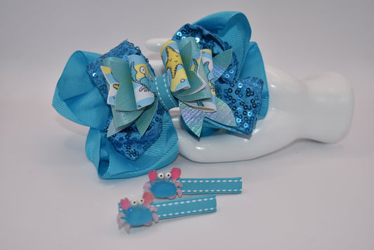 Get ready to make a splash with Nana's Collection! Our Under the Sea Bow features a playful crab-inspired design mixed with gorgeous blue and sparkle ribbons. This 3-piece set also includes two matching alligator clips for a complete look.
