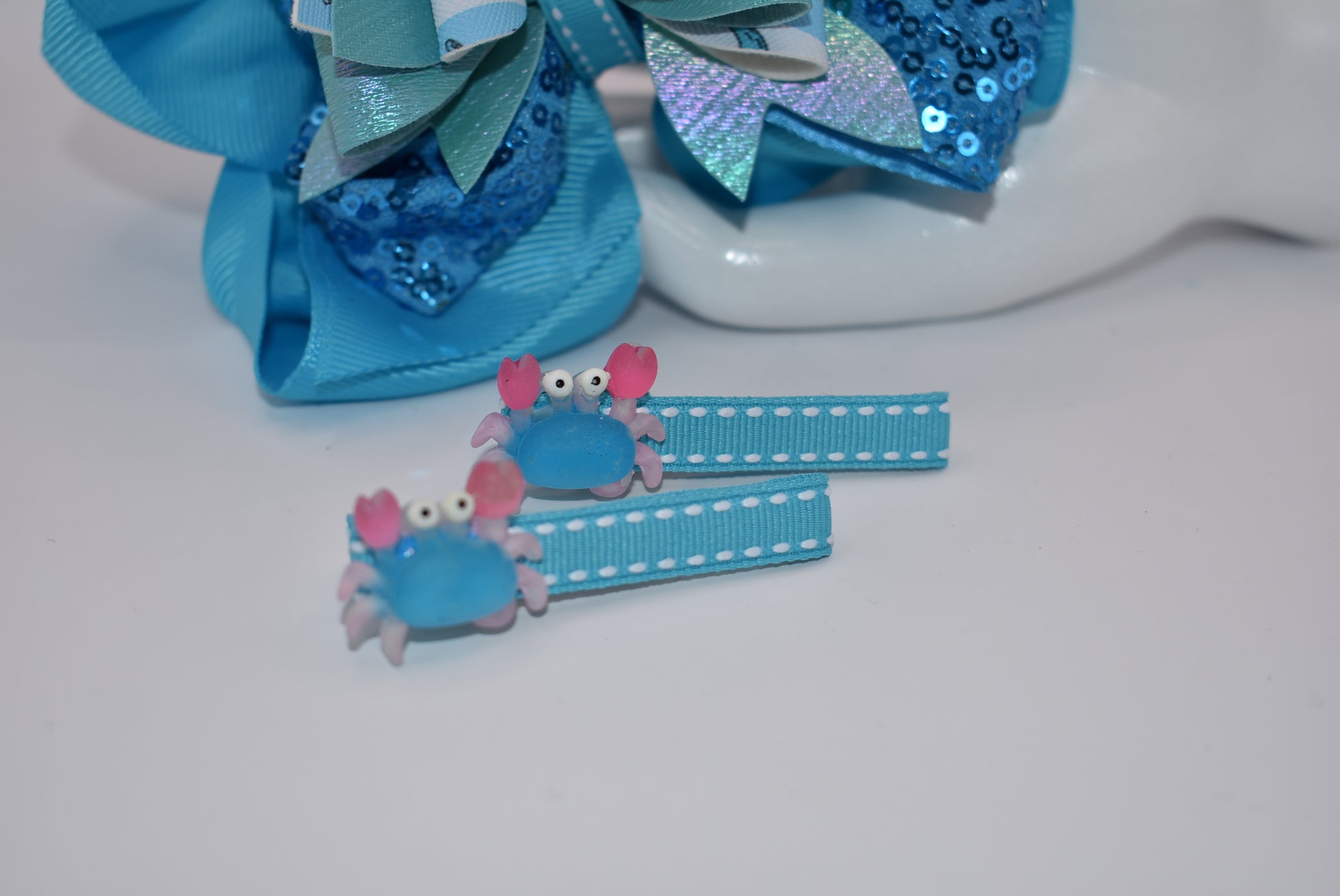 Get ready to make a splash with Nana's Collection! Our Under the Sea Bow features a playful crab-inspired design mixed with gorgeous blue and sparkle ribbons. This 3-piece set also includes two matching alligator clips for a complete look.