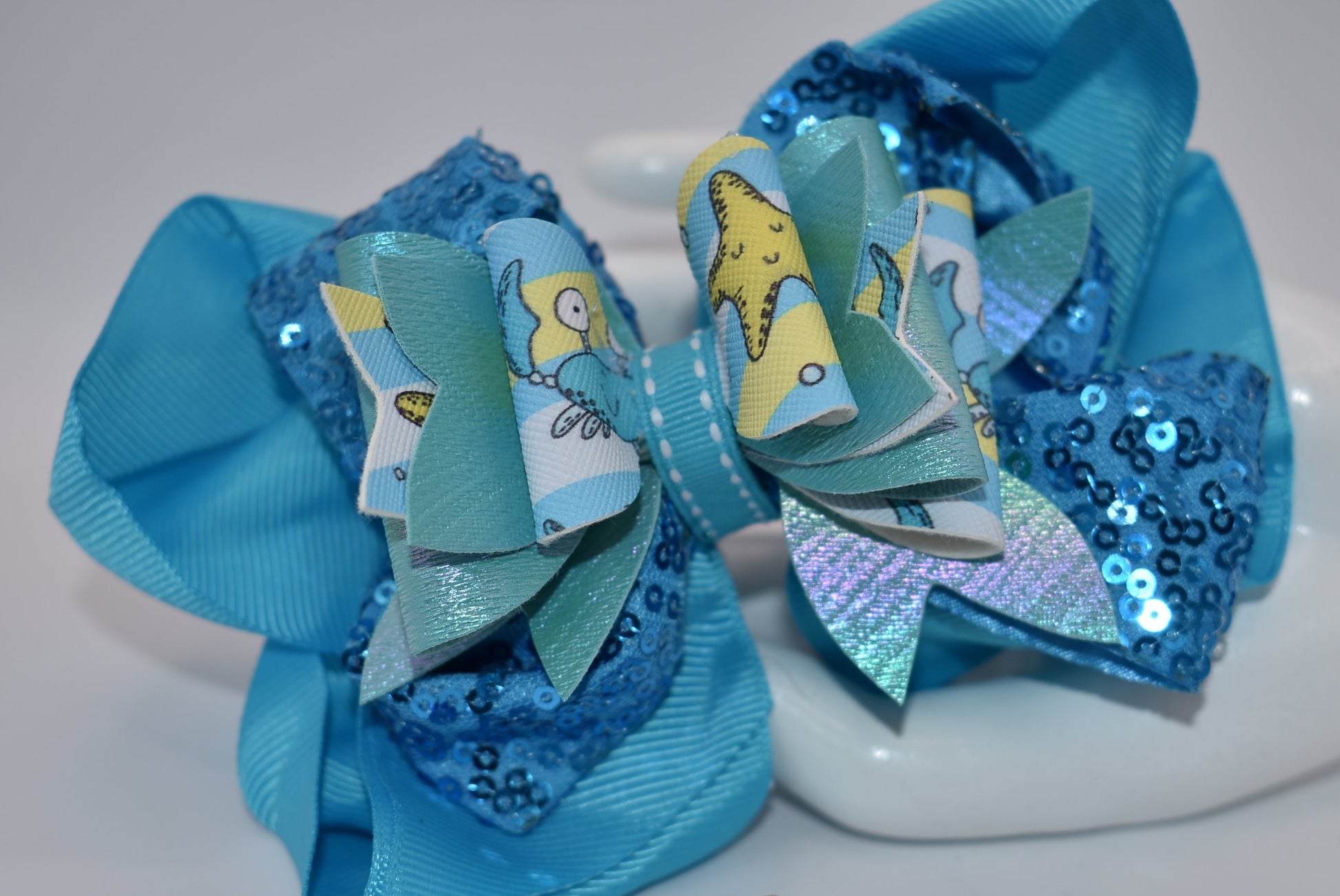Get ready to make a splash with Nana's Collection! Our Under the Sea Bow features a playful crab-inspired design mixed with gorgeous blue and sparkle ribbons. This 3-piece set also includes two matching alligator clips for a complete look.
