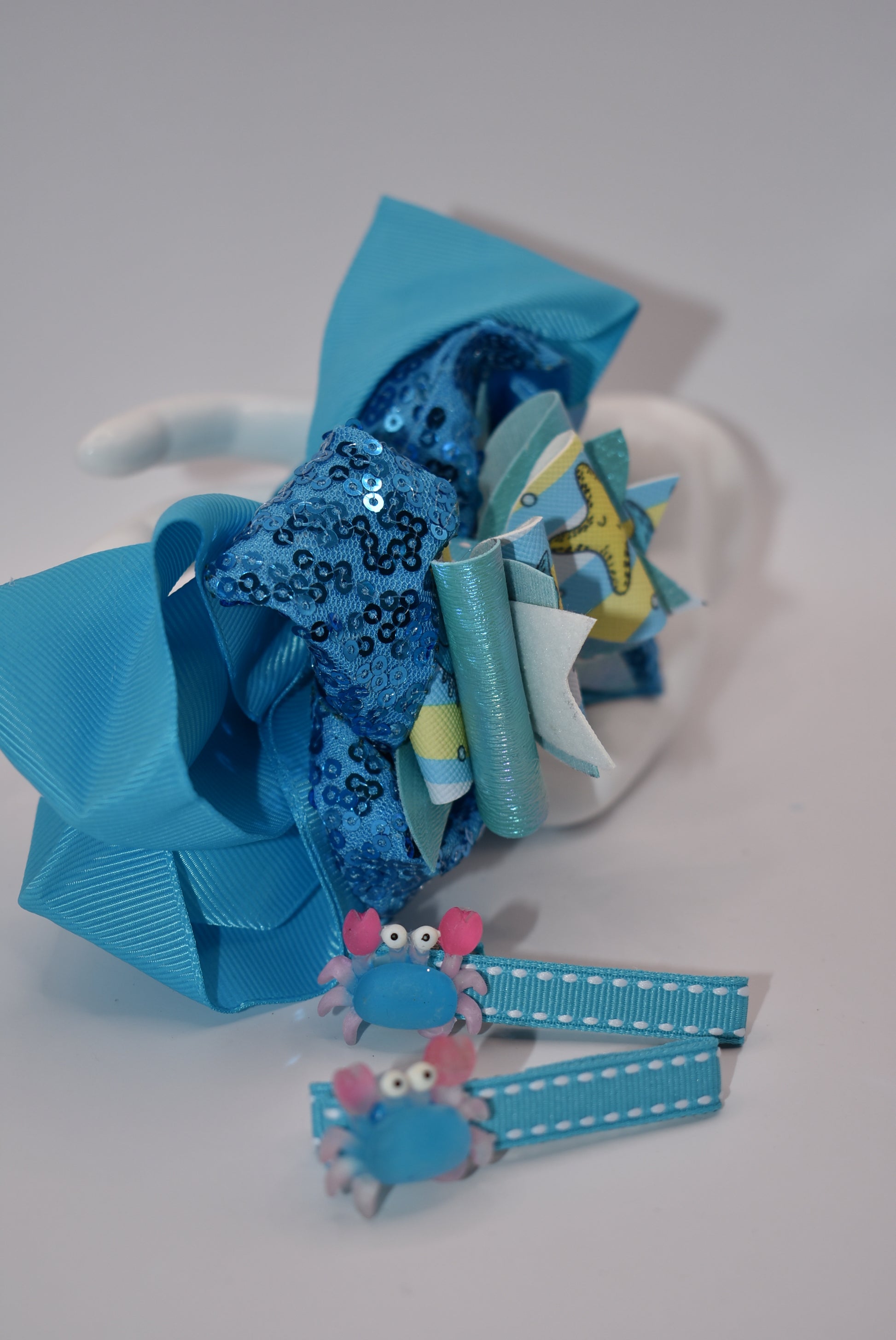 Get ready to make a splash with Nana's Collection! Our Under the Sea Bow features a playful crab-inspired design mixed with gorgeous blue and sparkle ribbons. This 3-piece set also includes two matching alligator clips for a complete look.