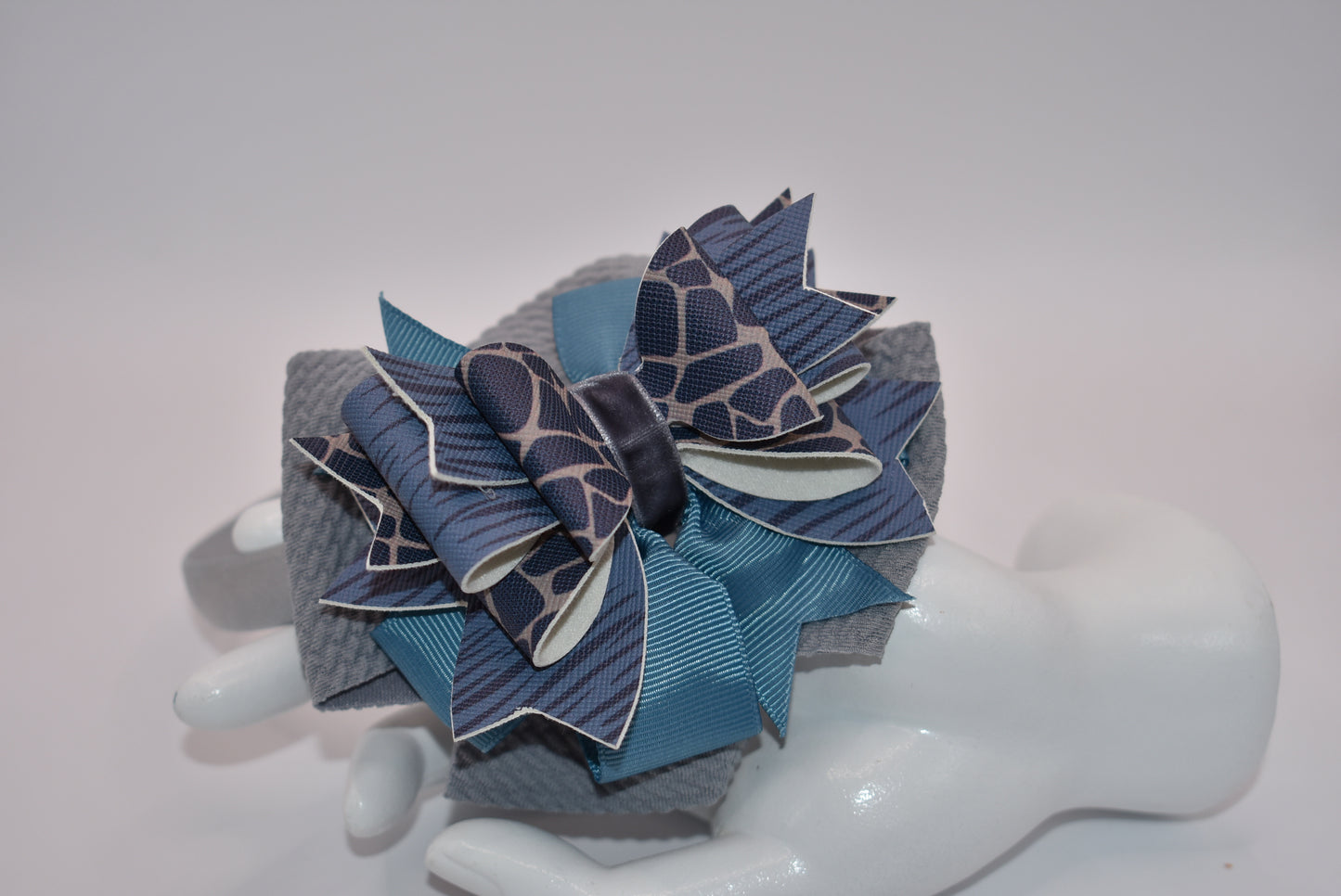 Add a little extra charm to your little one's style with Nana's Collection headband. The beautiful satin wrap holds layers of faux leather and ribbon in shades of blue and gray, making it a favorite accessory.