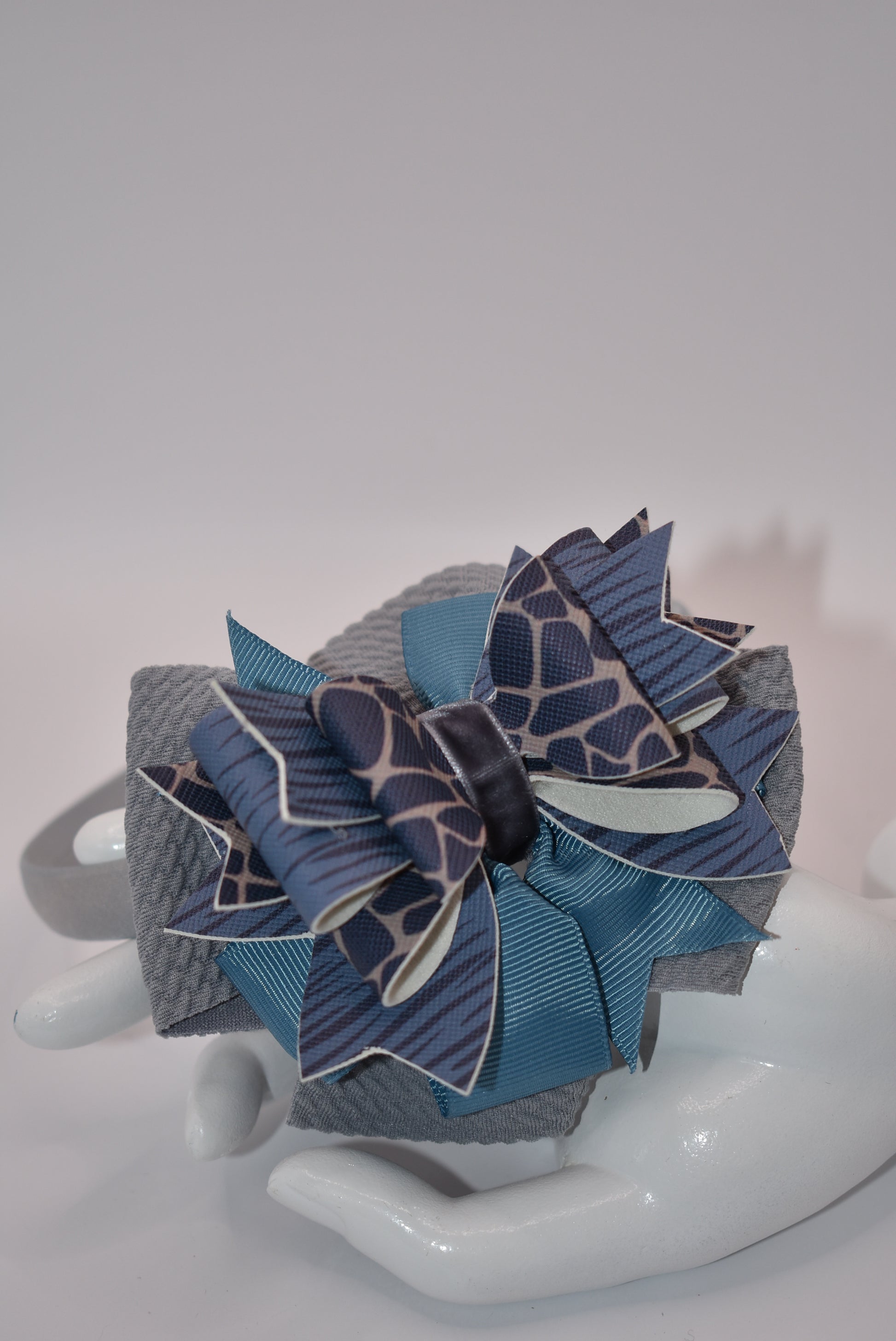 Add a little extra charm to your little one's style with Nana's Collection headband. The beautiful satin wrap holds layers of faux leather and ribbon in shades of blue and gray, making it a favorite accessory.