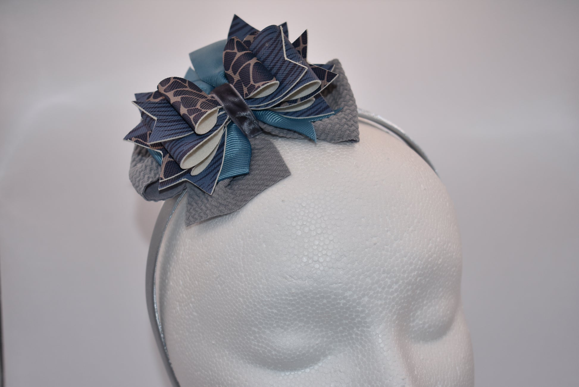 Add a little extra charm to your little one's style with Nana's Collection headband. The beautiful satin wrap holds layers of faux leather and ribbon in shades of blue and gray, making it a favorite accessory.