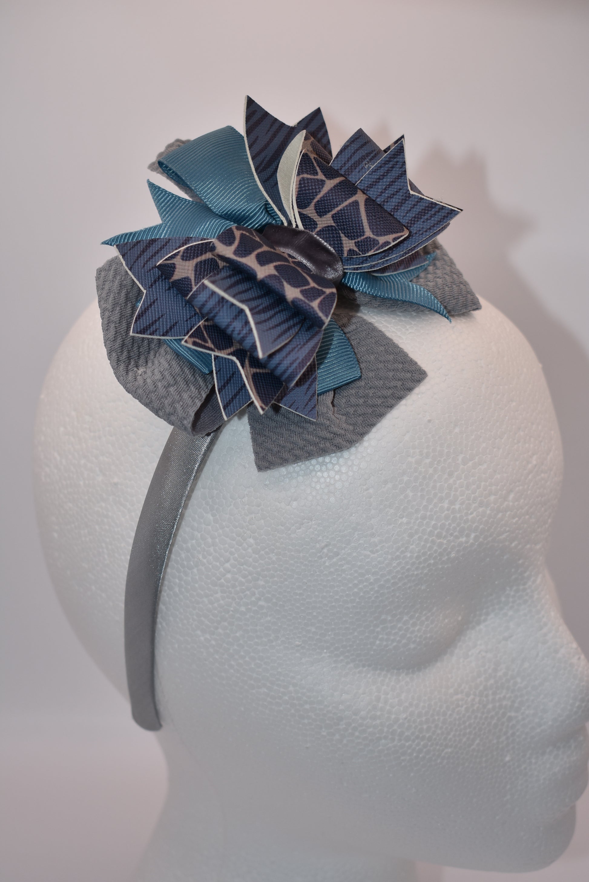 Add a little extra charm to your little one's style with Nana's Collection headband. The beautiful satin wrap holds layers of faux leather and ribbon in shades of blue and gray, making it a favorite accessory.