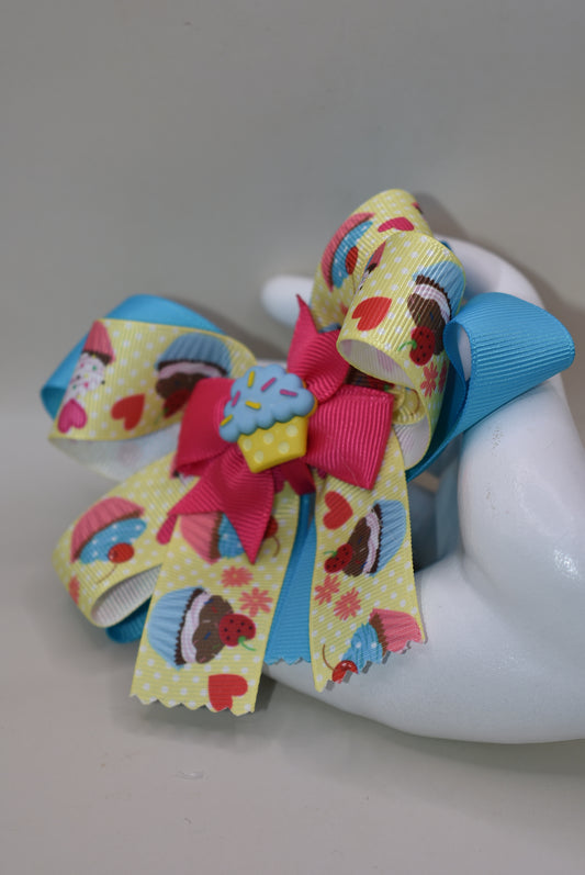 Indulge in Nana's Collection 71, featuring a playful bow with an adorable cupcake charm. The covered alligator clip makes for easy wear, perfect for any occasion. Satisfy your sweet tooth with this fun and quirky cupcake 