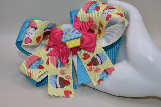 Indulge in Nana's Collection 71, featuring a playful bow with an adorable cupcake charm. The covered alligator clip makes for easy wear, perfect for any occasion. Satisfy your sweet tooth with this fun and quirky cupcake 