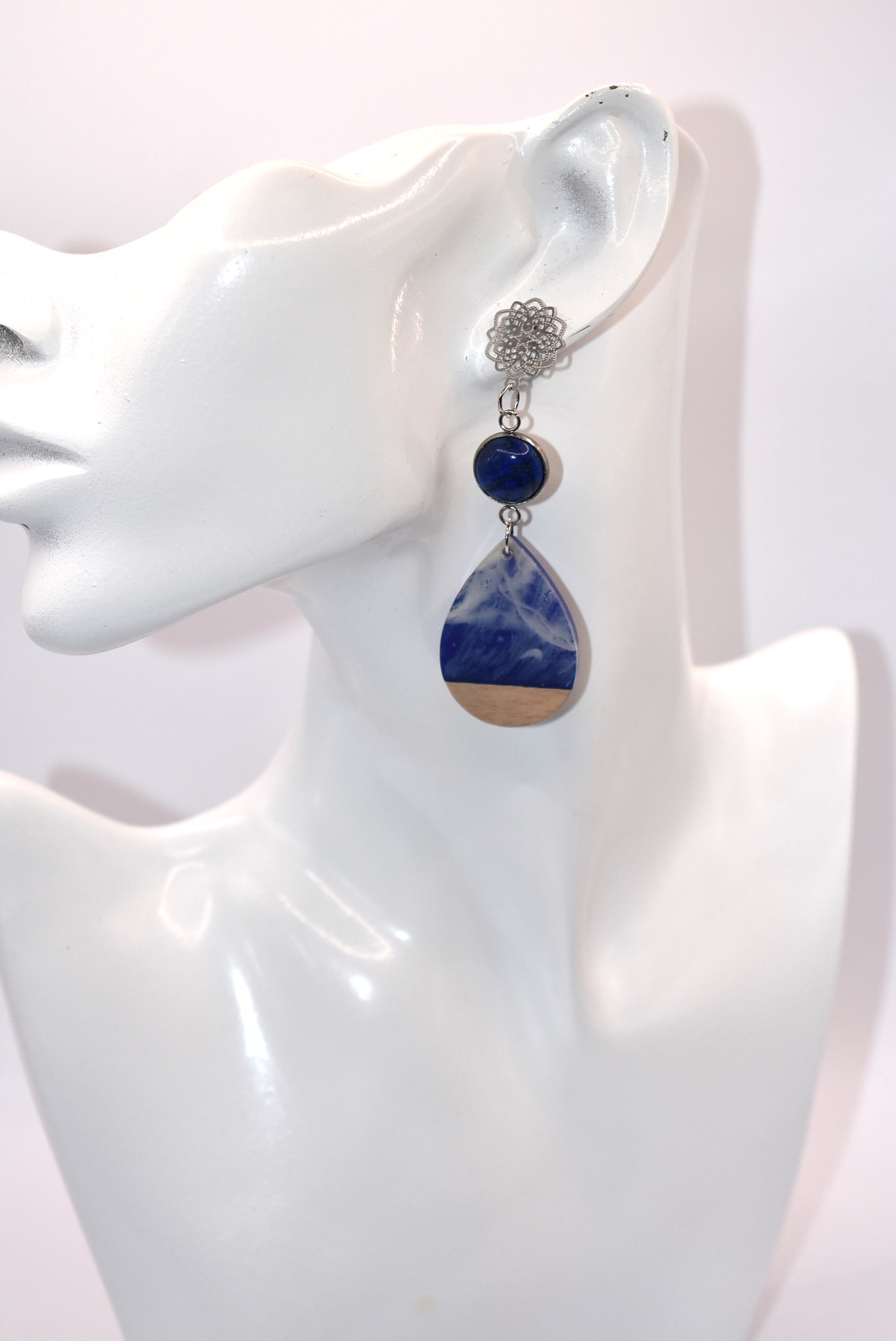 Unleash your unique style with the Blue Collection! This one-of-a-kind piece features a blue cabochon stone on a long silver filigree post, with a resin and wood teardrop that hangs around 2 1/2 inches for a chic look. Hypoallergenic posts make it super comfortable for sensitive ears.