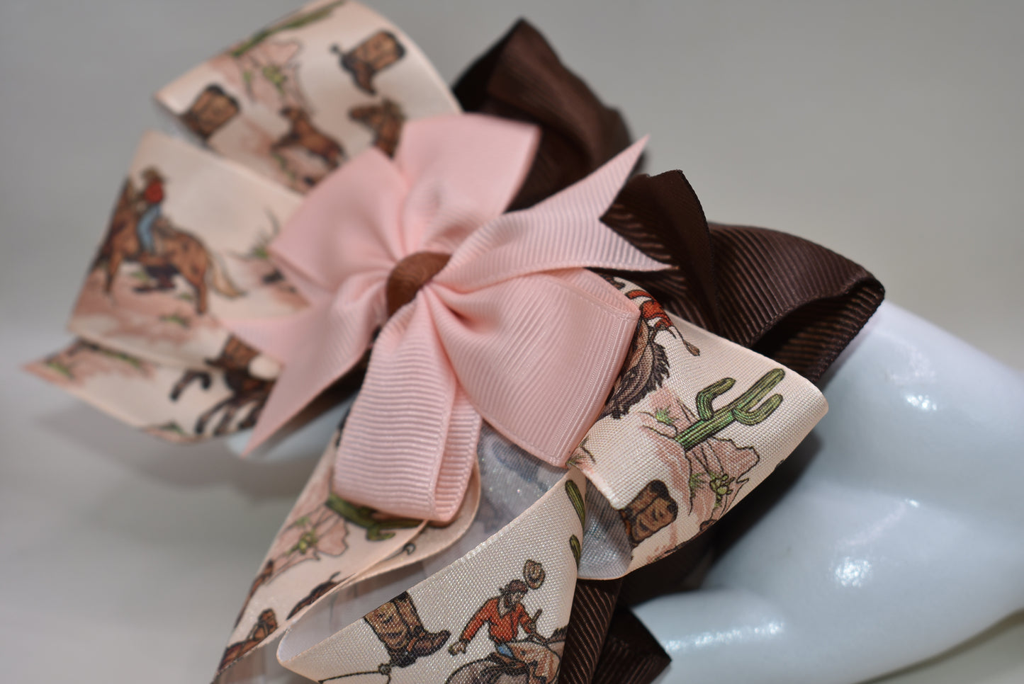 Add a splash of charm with this one-of-a-kind cowgirl bow! 🤠 A large brown grosgrain ribbon showcases a delicate cowgirl motif, topped with a sweet peach bow 🎀. Securely fastened with an alligator clip, it stays put while you shine! Perfect for little cowgirls ready to twirl and play. 🌟🐴
