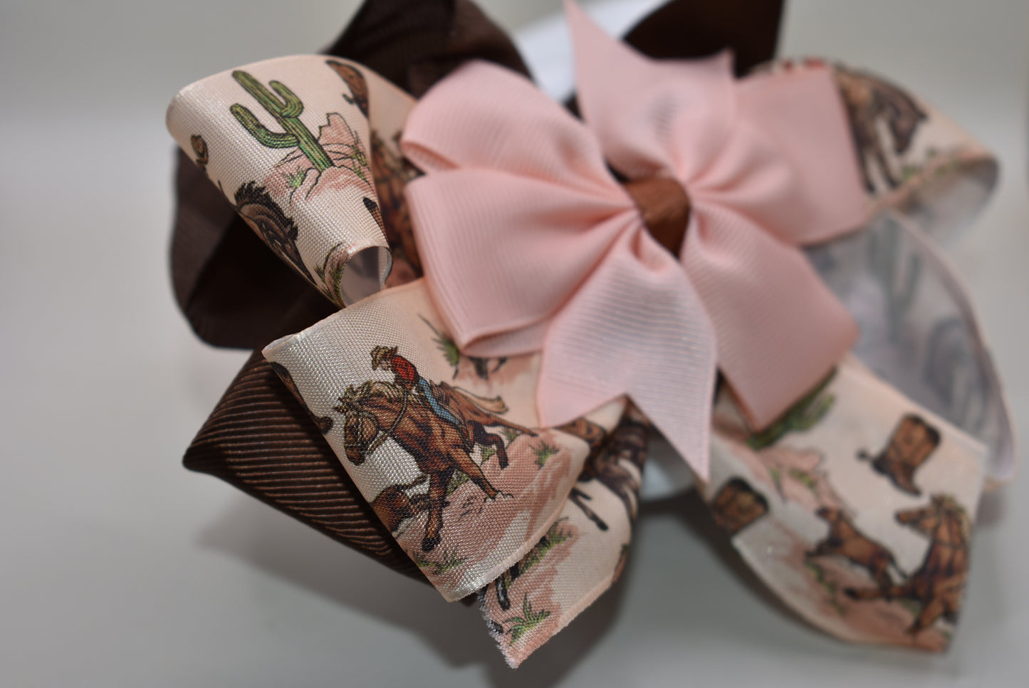 Add a splash of charm with this one-of-a-kind cowgirl bow! 🤠 A large brown grosgrain ribbon showcases a delicate cowgirl motif, topped with a sweet peach bow 🎀. Securely fastened with an alligator clip, it stays put while you shine! Perfect for little cowgirls ready to twirl and play. 🌟🐴