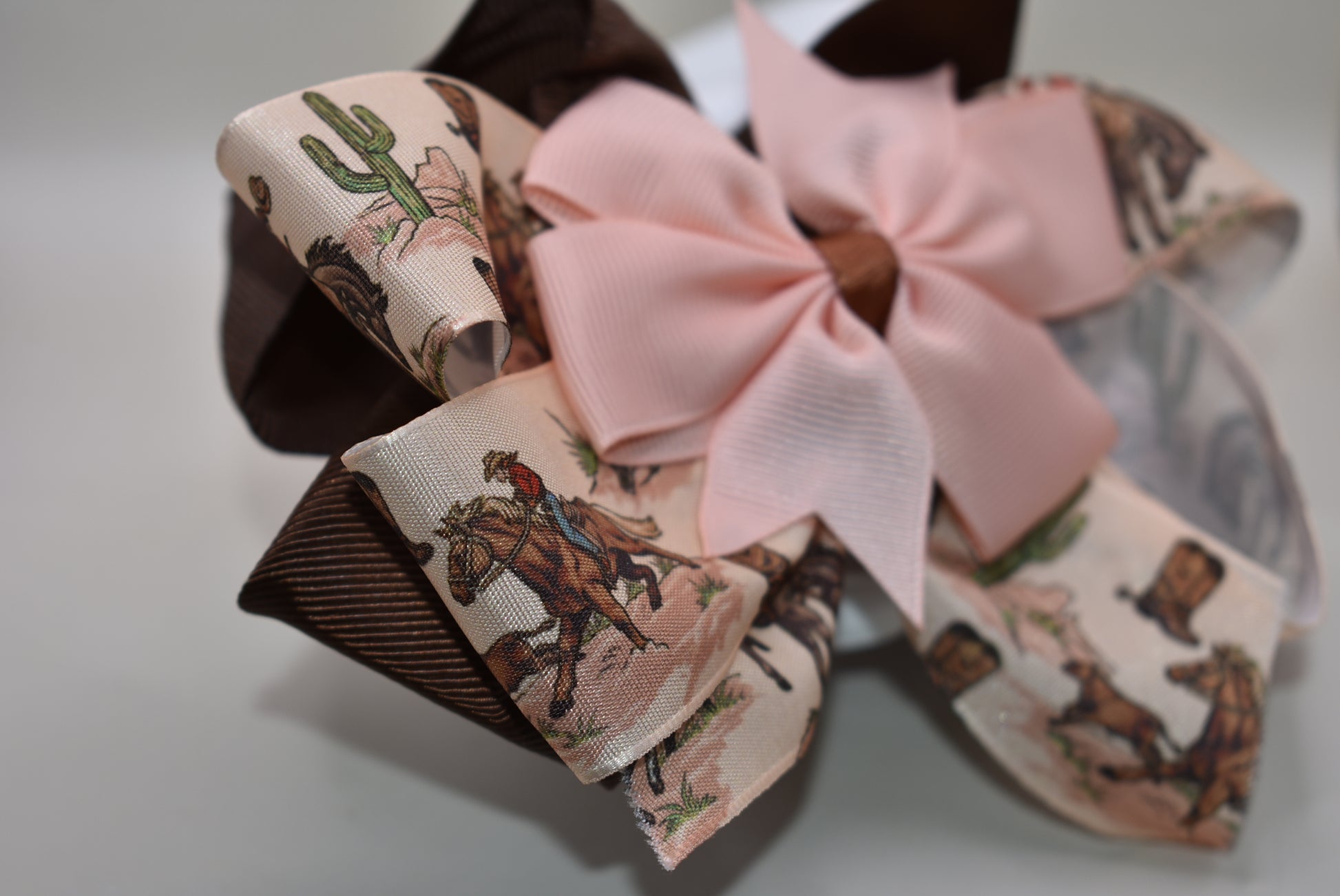 Add a splash of charm with this one-of-a-kind cowgirl bow! 🤠 A large brown grosgrain ribbon showcases a delicate cowgirl motif, topped with a sweet peach bow 🎀. Securely fastened with an alligator clip, it stays put while you shine! Perfect for little cowgirls ready to twirl and play. 🌟🐴