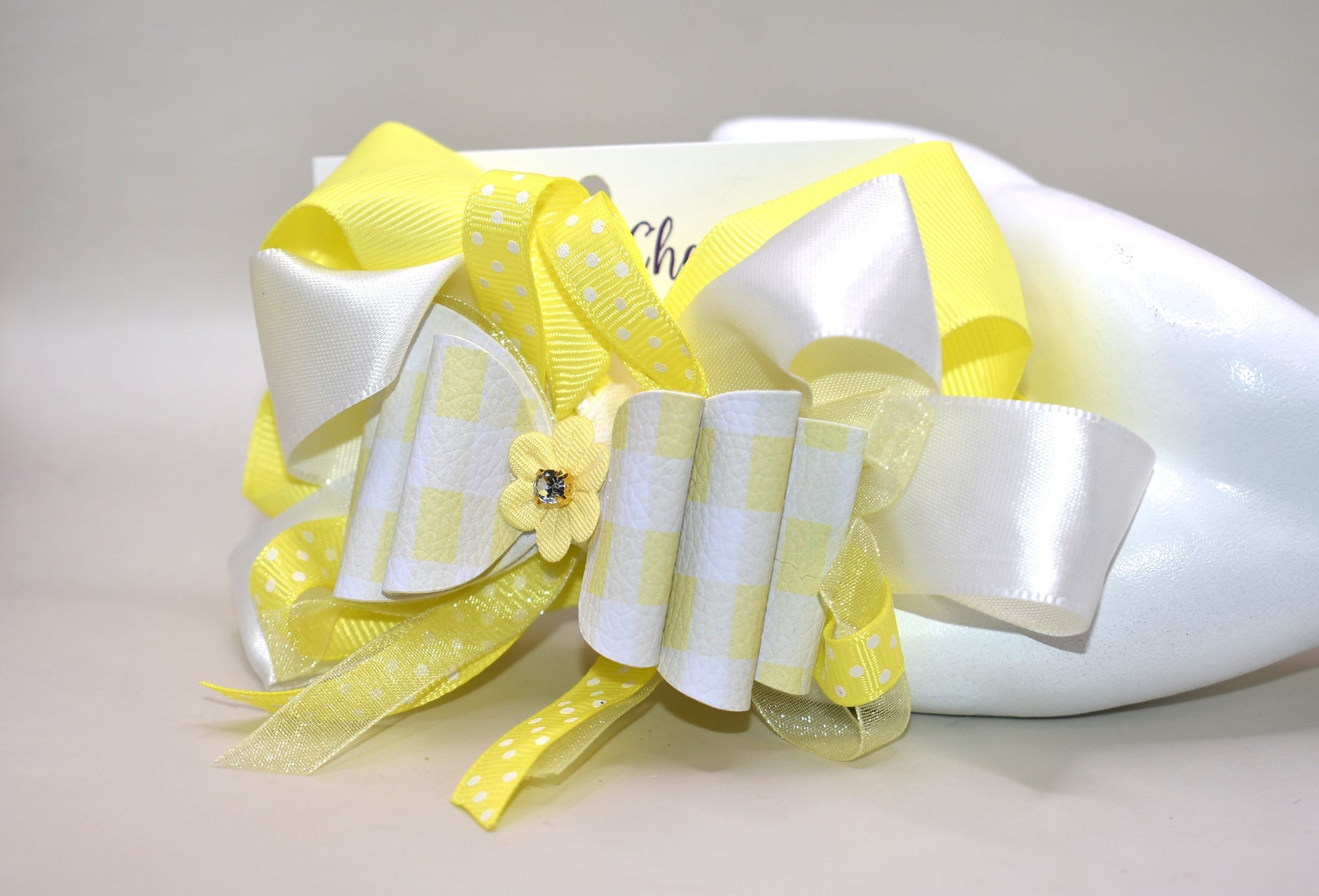 Add a splash of sunshine to your look with this playful hair clip from Nana's Collection 166. Featuring a cheerful mix of yellow and white ribbons accented with charming polka dots, it’s topped with a cute yellow flower and sparkling crystal for a touch of sparkle. The wrapped alligator clip ensures a secure hold, making it perfect for brightening any hairstyle with a fun, whimsical flair.