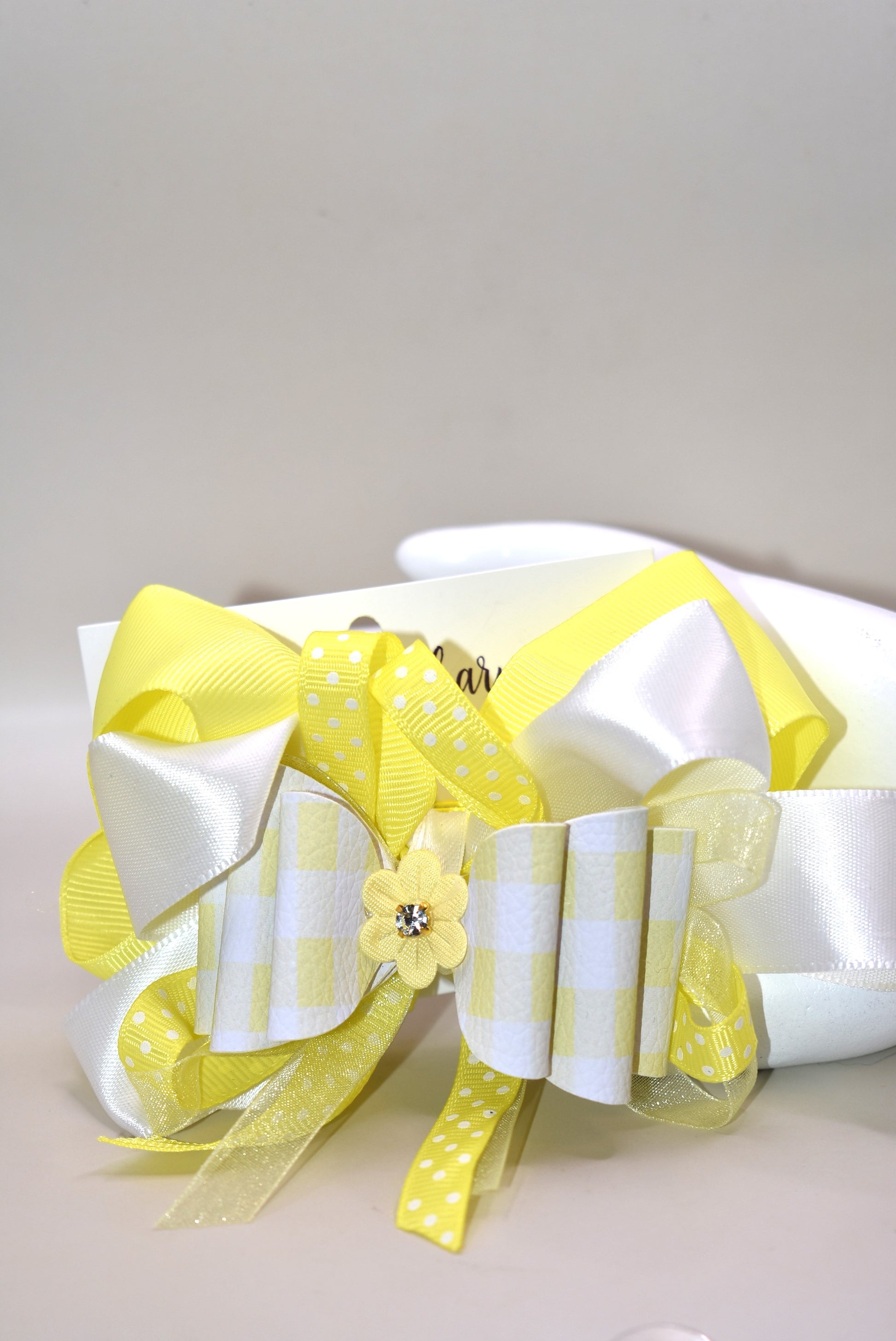 Add a splash of sunshine to your look with this playful hair clip from Nana's Collection 166. Featuring a cheerful mix of yellow and white ribbons accented with charming polka dots, it’s topped with a cute yellow flower and sparkling crystal for a touch of sparkle. The wrapped alligator clip ensures a secure hold, making it perfect for brightening any hairstyle with a fun, whimsical flair.