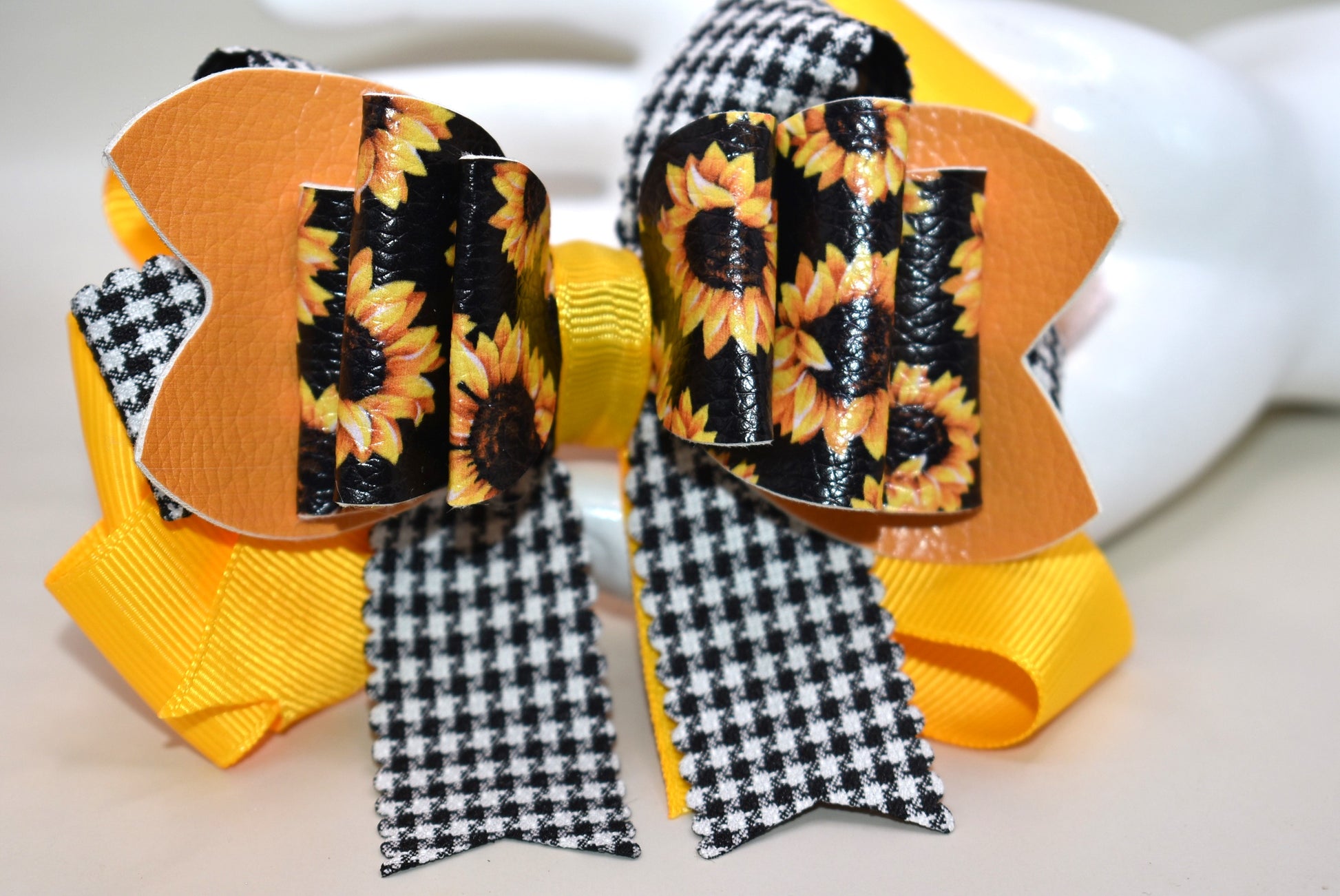 Brighten any outfit with this playful hair clip featuring a charming sunflower motif and layers of pretty ribbon. The black and white checkered ribbon adds a fun touch, while the wrapped alligator clip ensures a secure fit all day long. Perfect for adding a splash of sunshine wherever you go! 🌻🎀🖤🤍