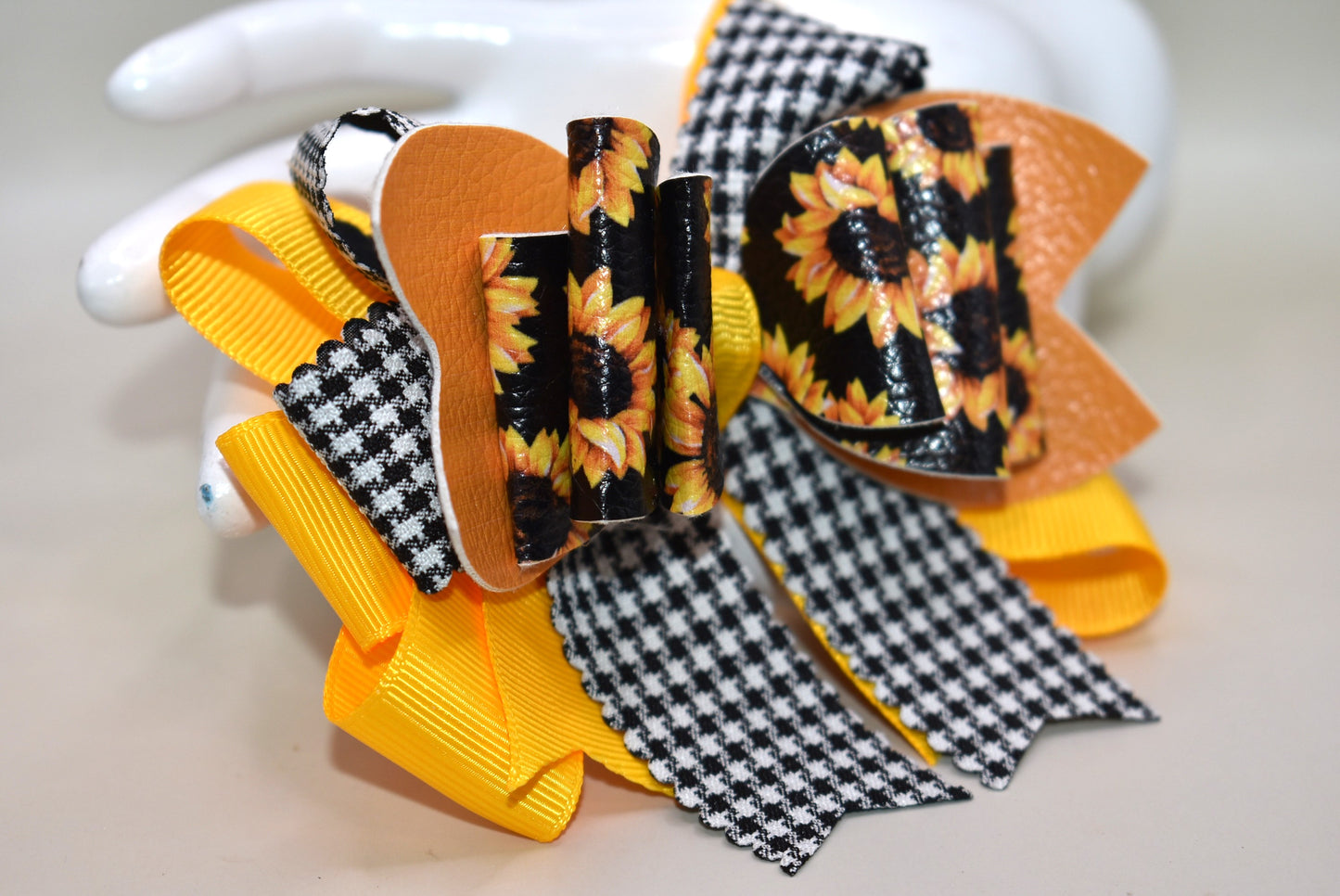 Brighten any outfit with this playful hair clip featuring a charming sunflower motif and layers of pretty ribbon. The black and white checkered ribbon adds a fun touch, while the wrapped alligator clip ensures a secure fit all day long. Perfect for adding a splash of sunshine wherever you go! 🌻🎀🖤🤍