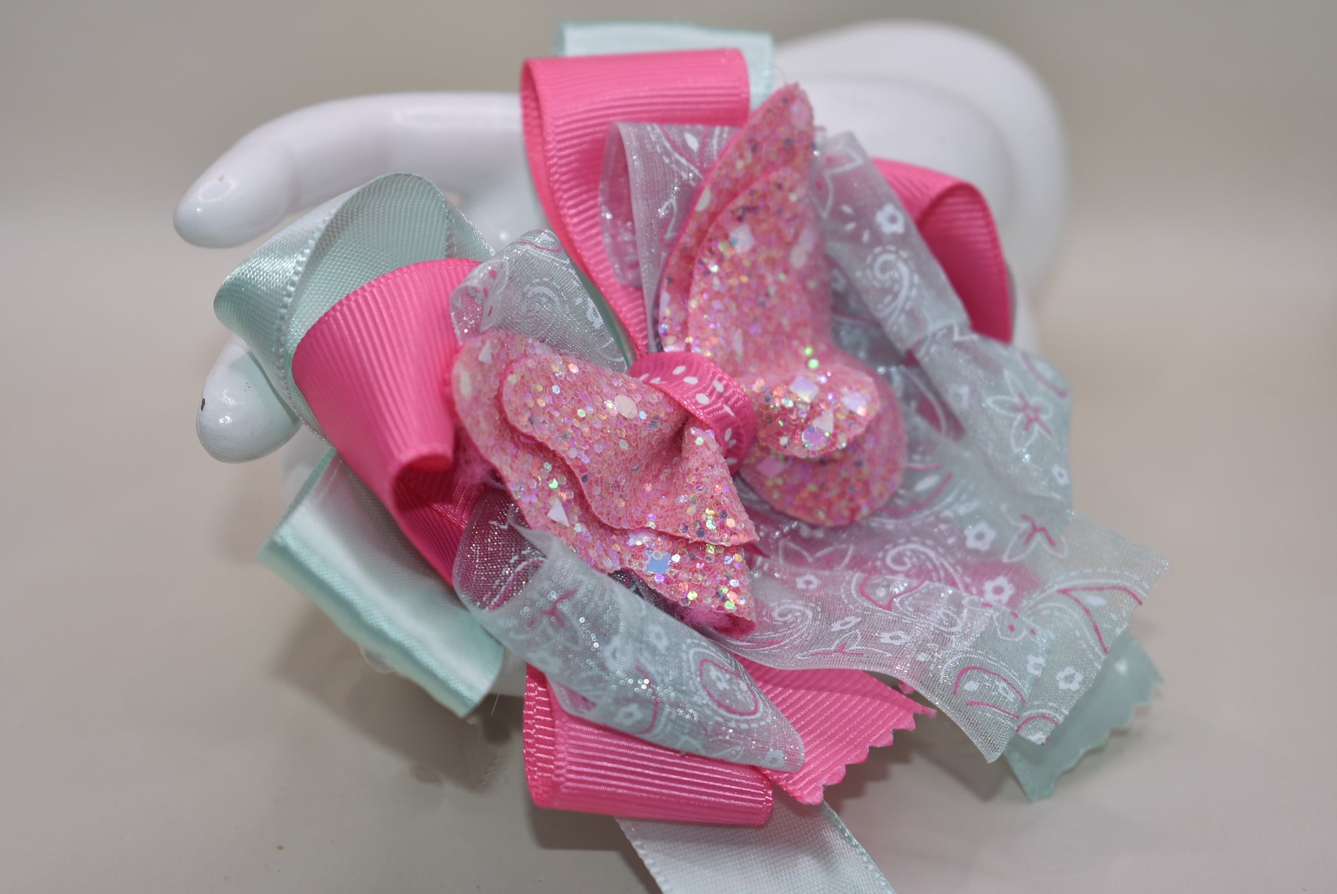 Add a touch of magic with this glittery butterfly perched atop a delicate mint green and pink ribbon. The comfy alligator clip keeps it secure, making it perfect for your little one to wear all day. Pretty, elegant, and absolutely adorable—watch her fall in love and never want to take it off! 🦋💚🎀