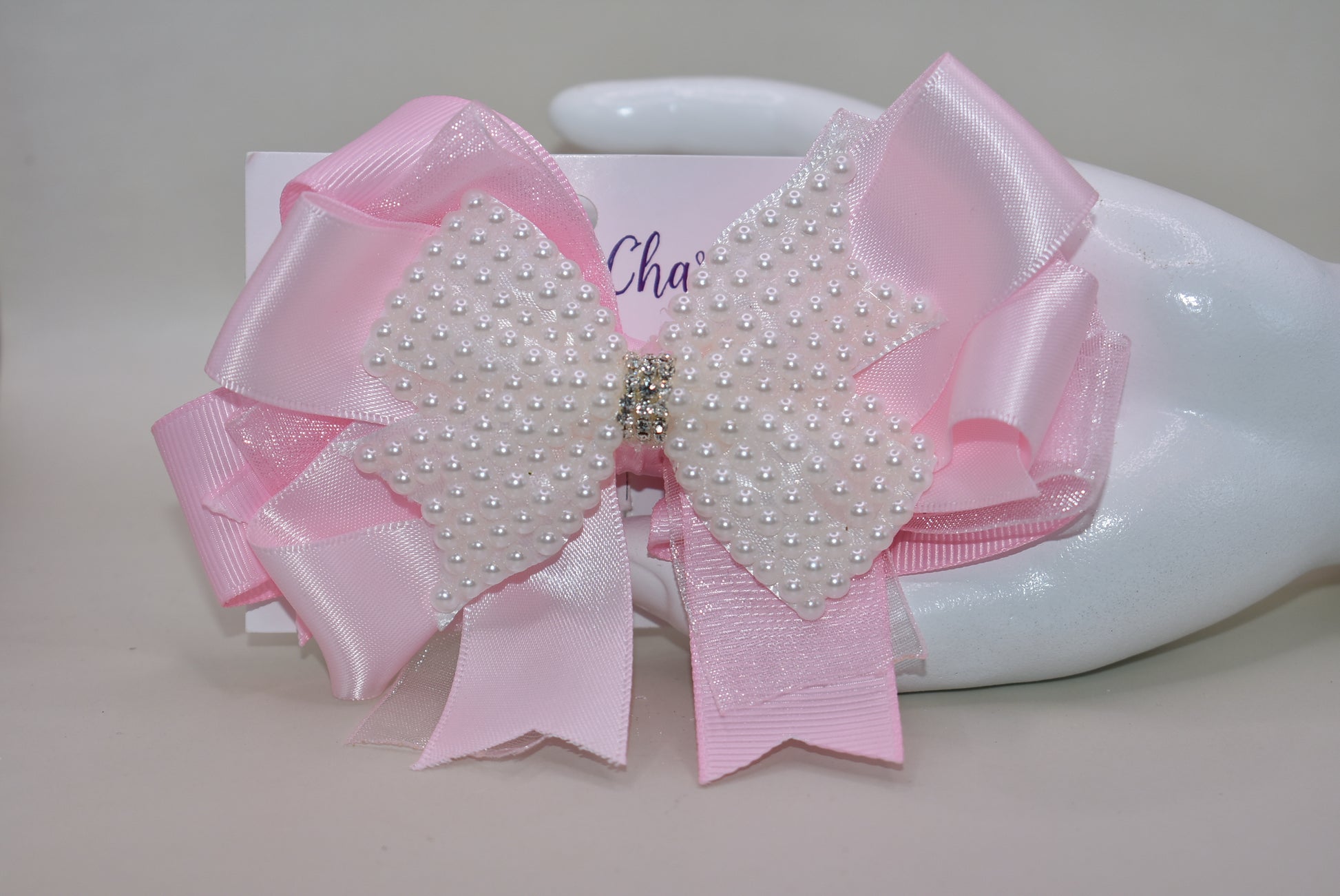 Add a splash of charm with this beautiful pink bow from Nana's Collection! 🌸 Layers of soft pink ribbons create a perfect princess look, topped with a sparkling pearl and crystal wrap ✨. The wrapped alligator clip makes it super easy to wear all day long. Perfect for the little girl who loves everything pink and pretty! 🎀💕