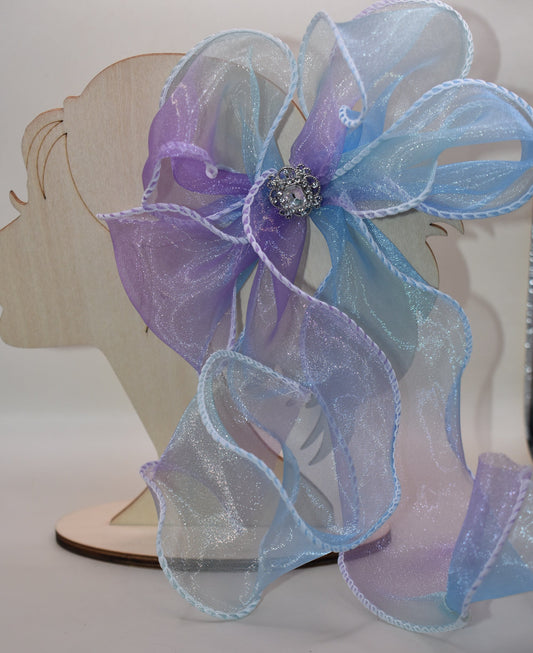 Elevate your style with this exquisite purple and blue sheer bow featuring a graceful fishtail edge. Long and elegant, it effortlessly adds a refined touch to any outfit. Secured with a wrapped alligator clip for easy wear, it is adorned with a delicate silver gem charm that completes its sophisticated appeal.