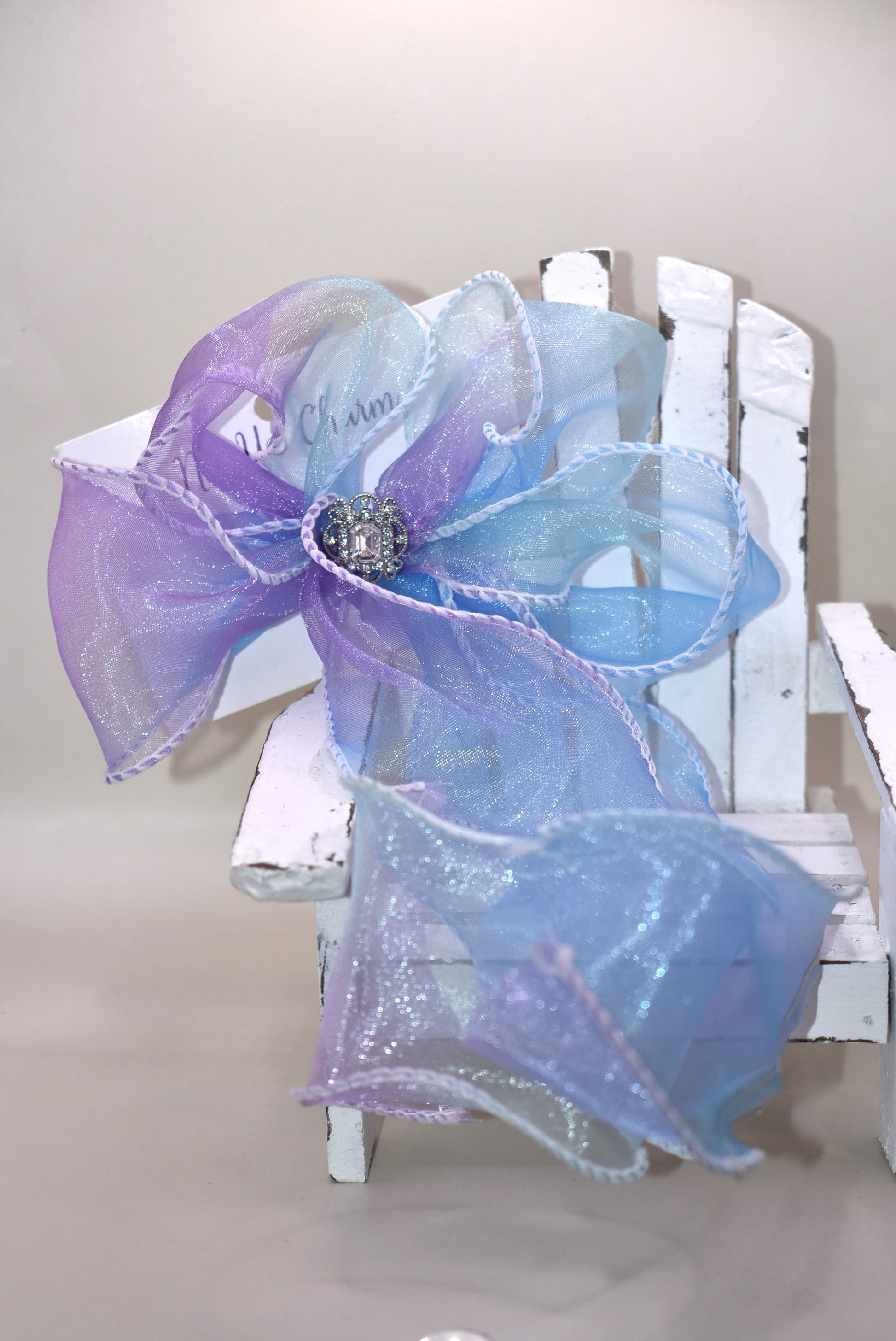 Elevate your style with this exquisite purple and blue sheer bow featuring a graceful fishtail edge. Long and elegant, it effortlessly adds a refined touch to any outfit. Secured with a wrapped alligator clip for easy wear, it is adorned with a delicate silver gem charm that completes its sophisticated appeal.