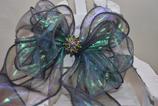 This elegant bow features an iridescent fishtail ribbon in stunning ocean hues, accented by a delicate crystal flower for a refined finish. Its long, flowing design adds graceful movement, while the wrapped alligator clip ensures a secure and comfortable fit. Perfect for adding a touch of sophistication to any look.