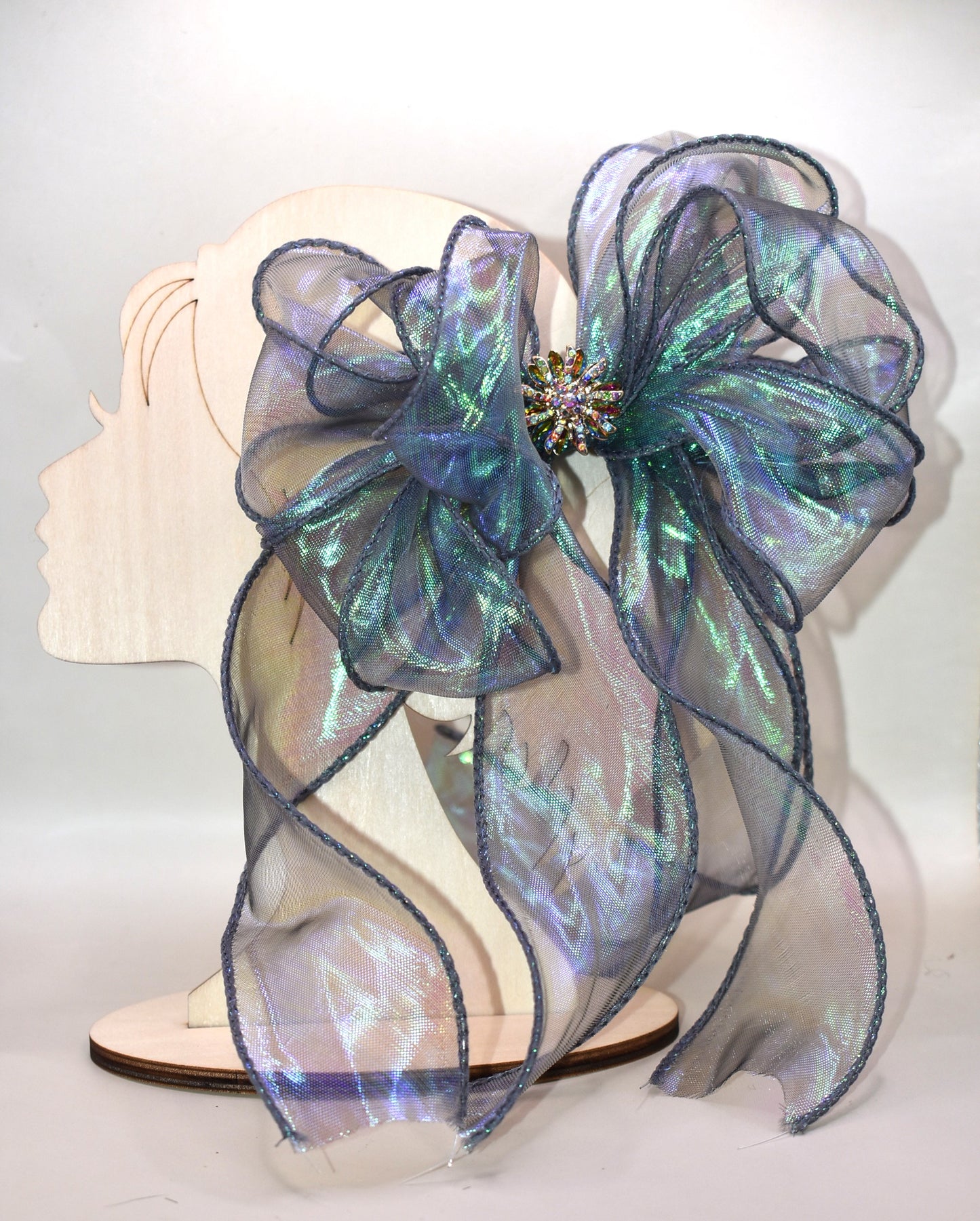 This elegant bow features an iridescent fishtail ribbon in stunning ocean hues, accented by a delicate crystal flower for a refined finish. Its long, flowing design adds graceful movement, while the wrapped alligator clip ensures a secure and comfortable fit. Perfect for adding a touch of sophistication to any look.