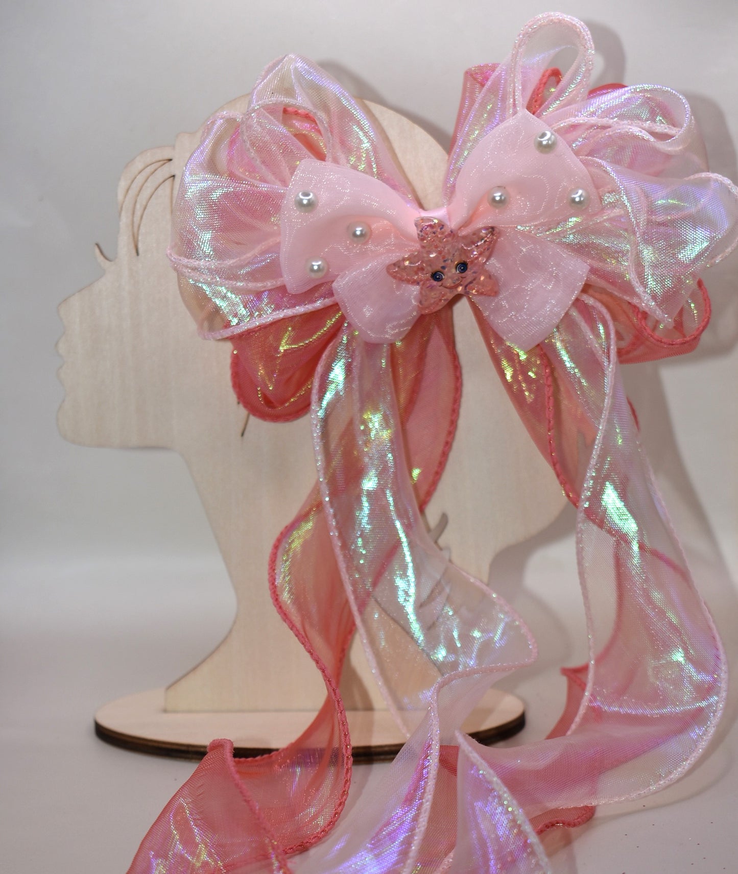 Dive into charm with this ocean-inspired long tail bow! 🌊 Layers of iridescent and sheer ribbons create a magical shimmer, topped with a delicate pearl chiffon bow 🎀. A sparkly starfish charm ✨ adds the perfect touch of seaside sparkle. Easy to wear with a wrapped alligator clip on the back. Fall head over fins for this beauty! 🐚💙